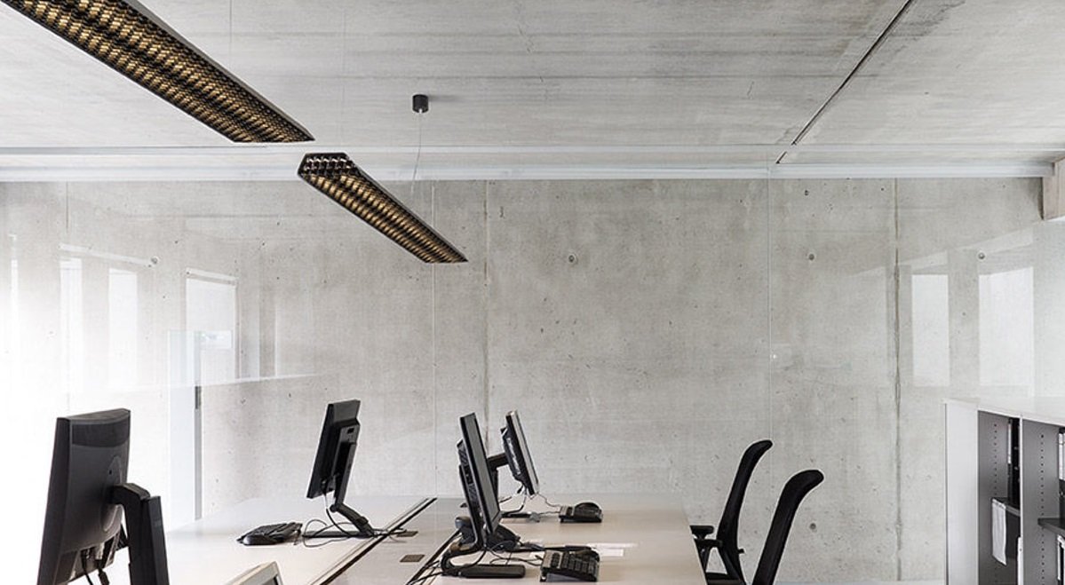 Leeres Büro mit Schreibtischen, Monitoren, Telefonen und schwarzen Bürostühlen, weiße Wände und große Fenster, moderne Beleuchtung.