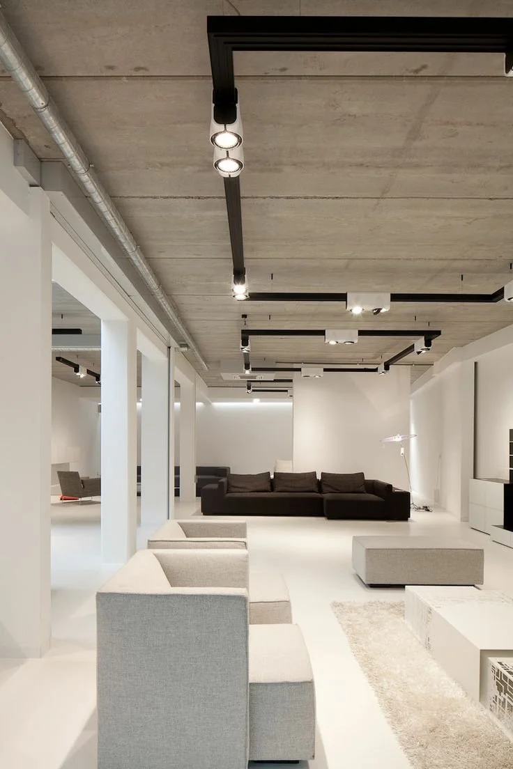 Modernes, minimalistisches Wohnzimmer mit weißen Wänden, schwarzen und grauen Sofas, und einer Decke mit schwarzen Lichtleisten.