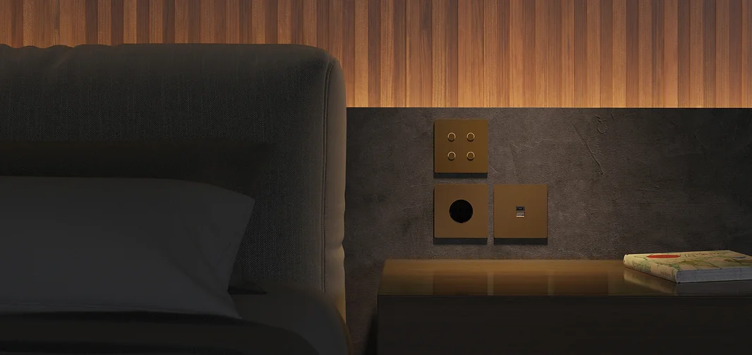 Nahaufnahme eines Nachttischs mit einer Lampe, eine Zeitschrift, und drei quadratischen Steckdosen an der Wand.