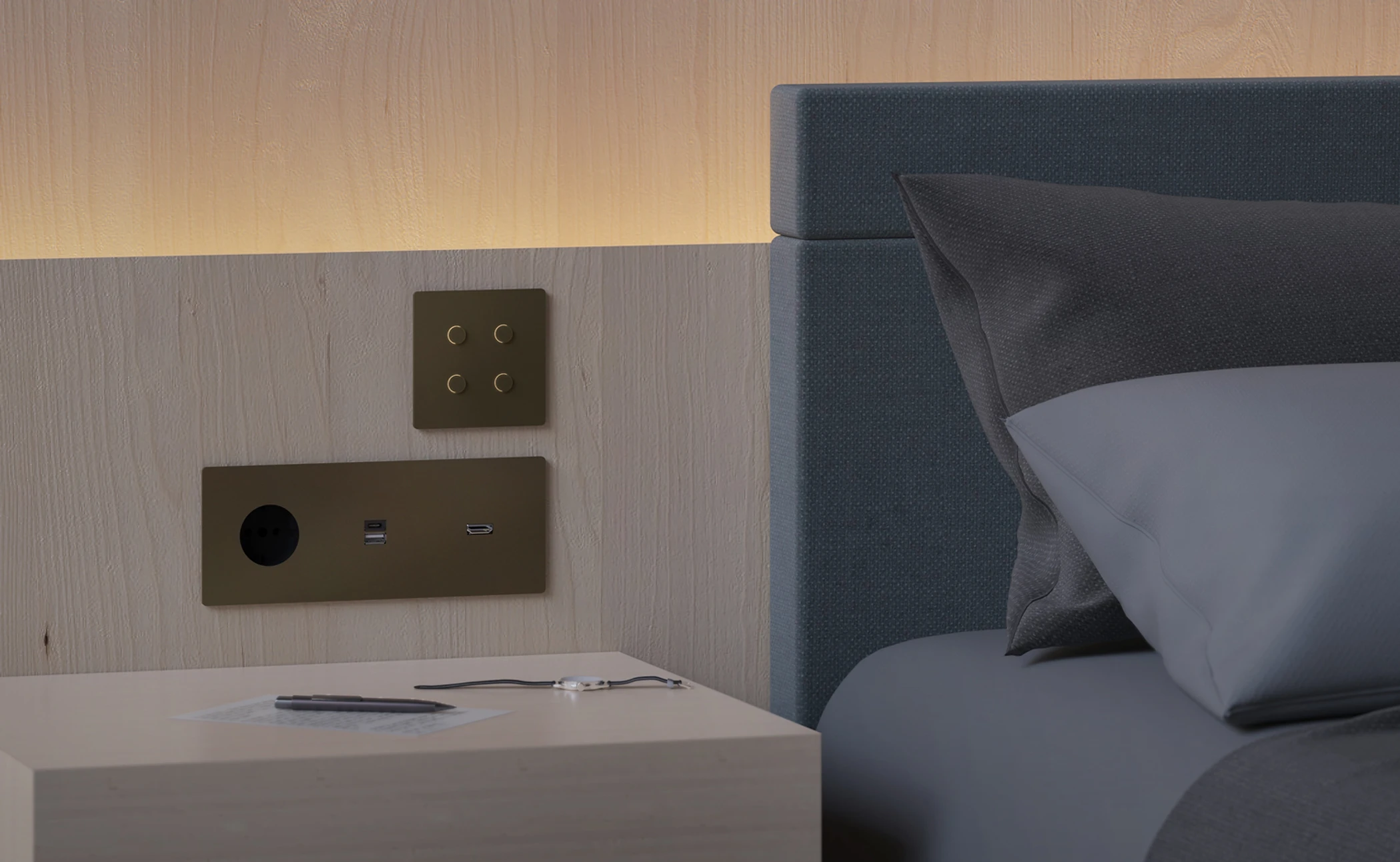 Nahaufnahme eines Hotelkopfteils mit Steckdosen, USB-Anschlüssen, einem Lichtschalter, einem Notizzettel, einem Kugelschreiber, einem Fenster und einem Bett mit schwarzen und grauen Kissen.