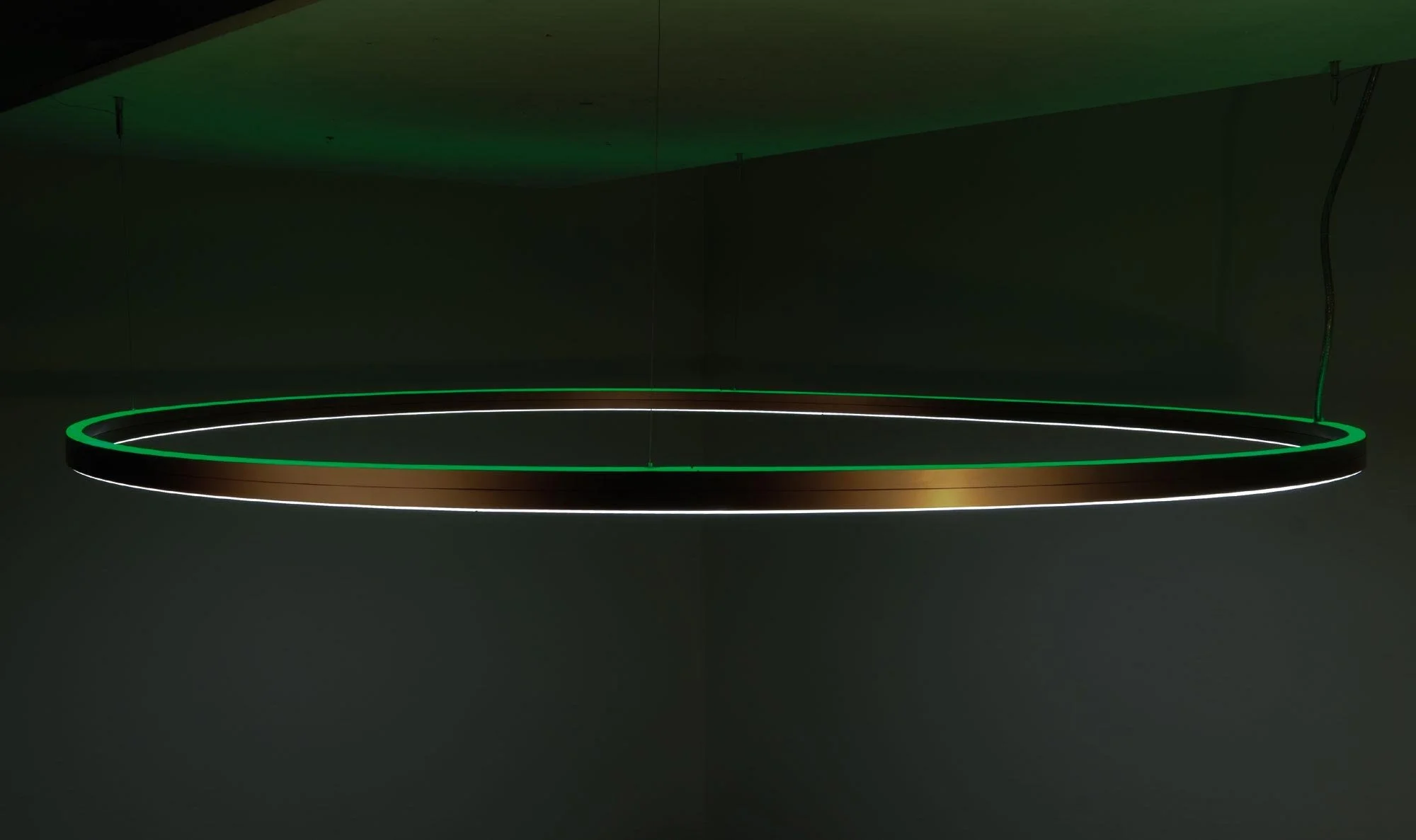 Moderne, kreisrunde Deckenleuchte mit grüner und weißer Lichtleiste, hängend an der Decke in einem dunklen Raum.