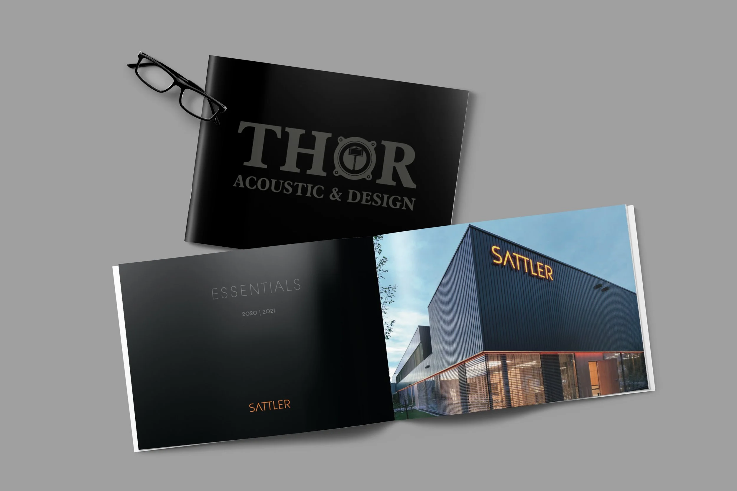 Ein schwarzes Magazin mit der Aufschrift 'THOR Acoustic & Design', ein geöffnetes Branchenbuch mit der Überschrift 'Essentials 2020/2021', und eine Broschüre mit einem modernen Gebäudefoto und dem Schriftzug 'SATTLER'