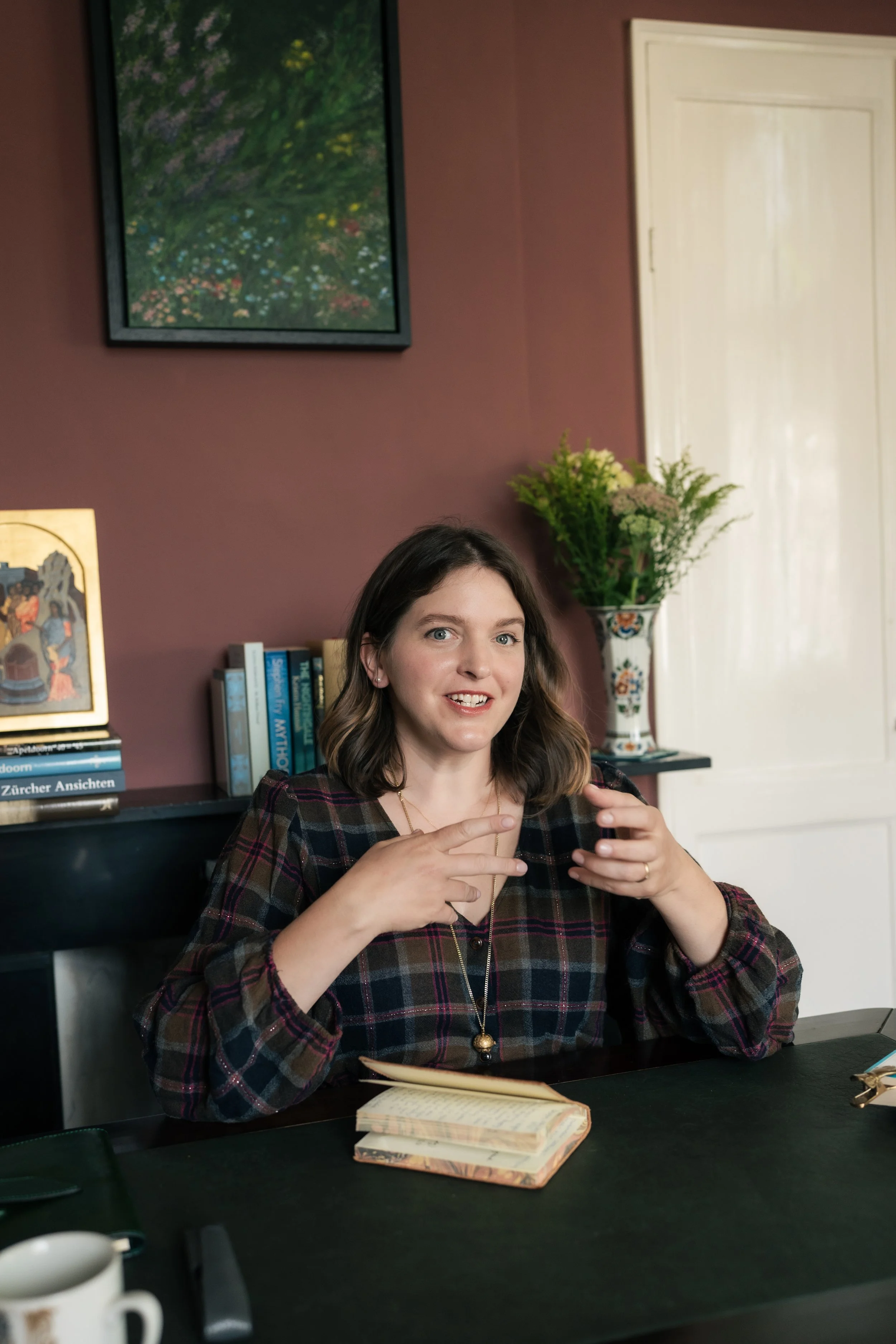 Nora Keller is sitting at her desk in her library, gesturing mid-explanation.