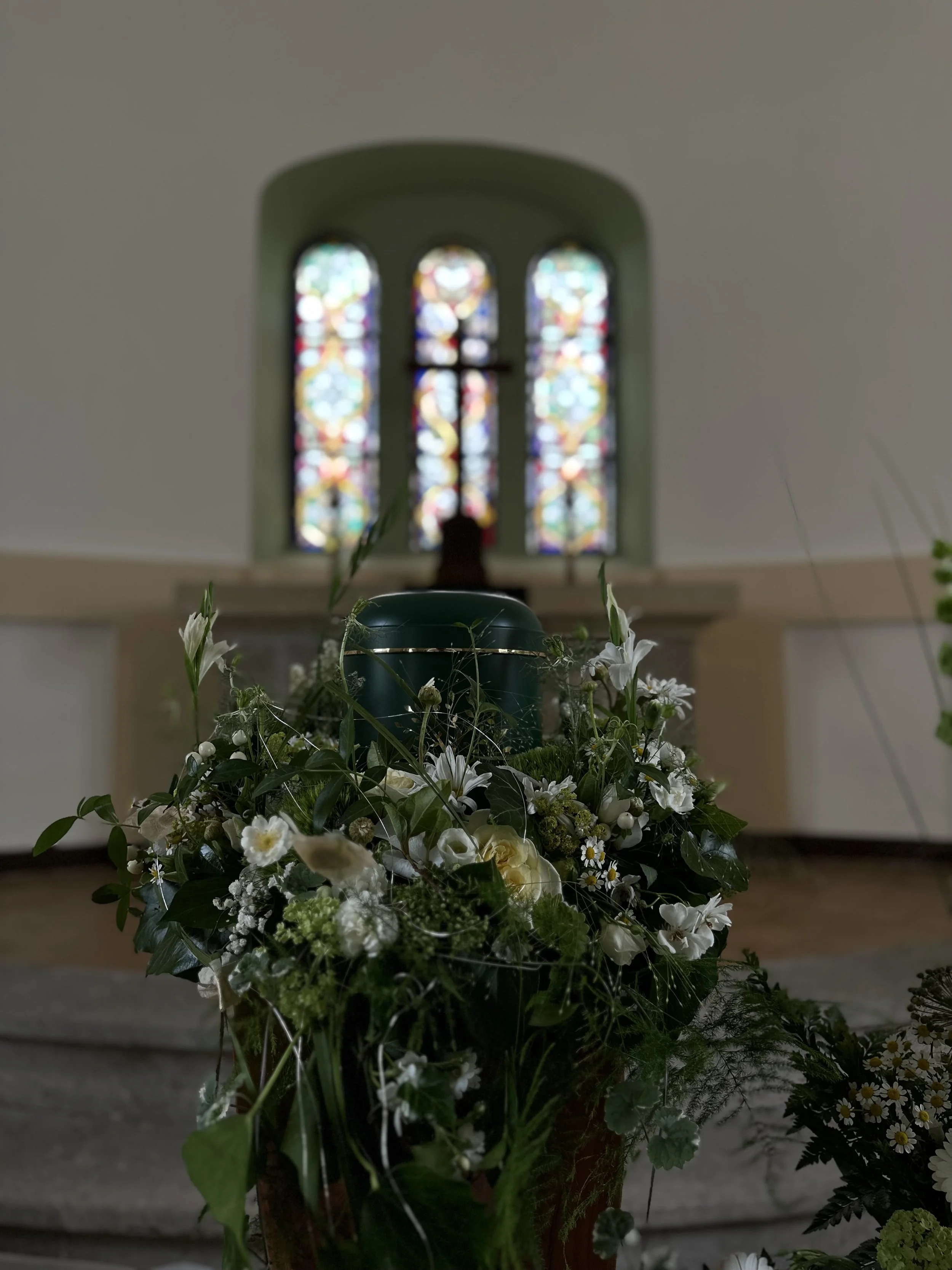 Blumenstrauß mit weißen und grünen Blumen vor einem bunten, gotischen Kirchenfenster
