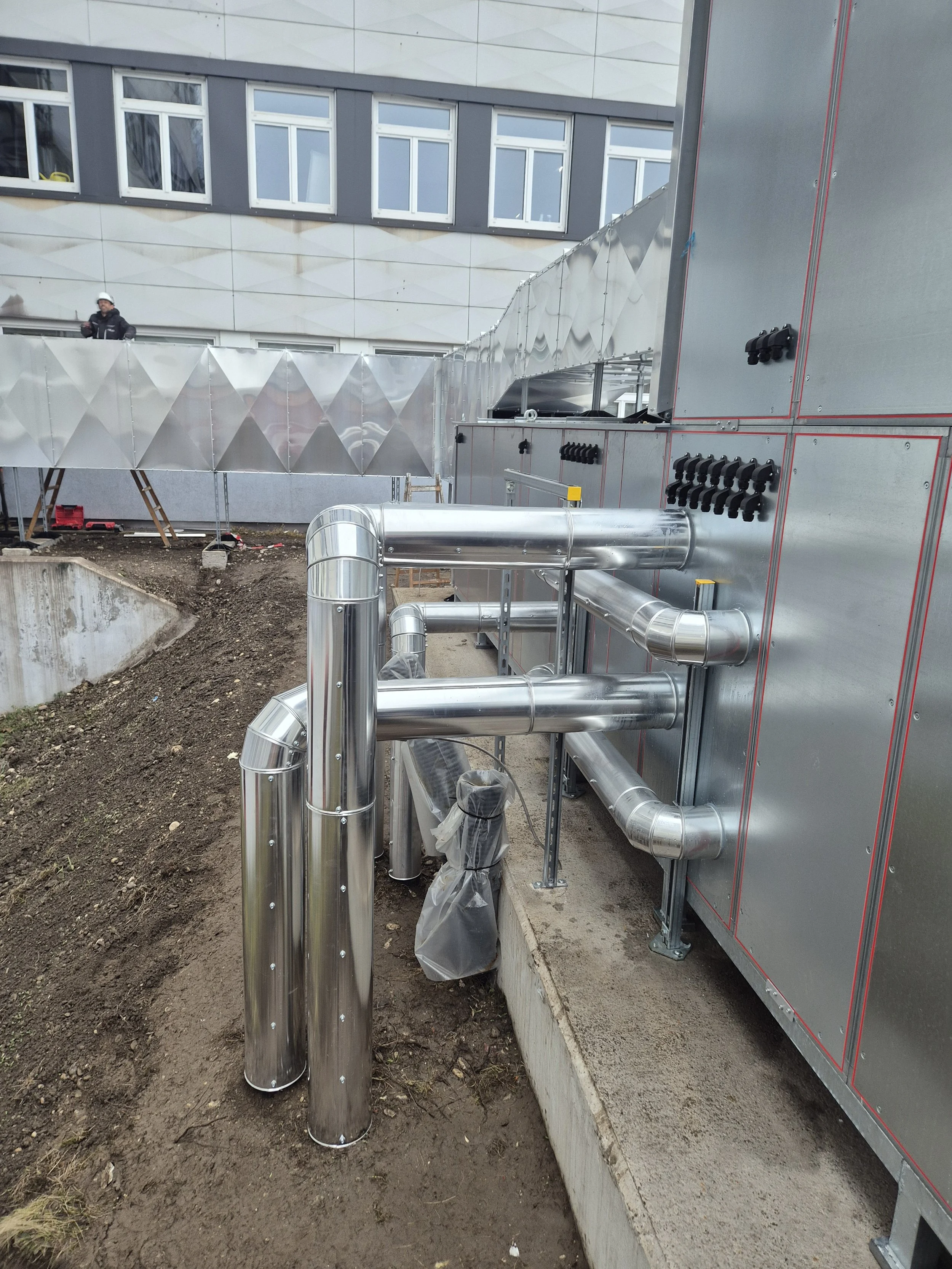 Baustelle mit Rohren und Gebäudefassade, dort wird gearbeitet.