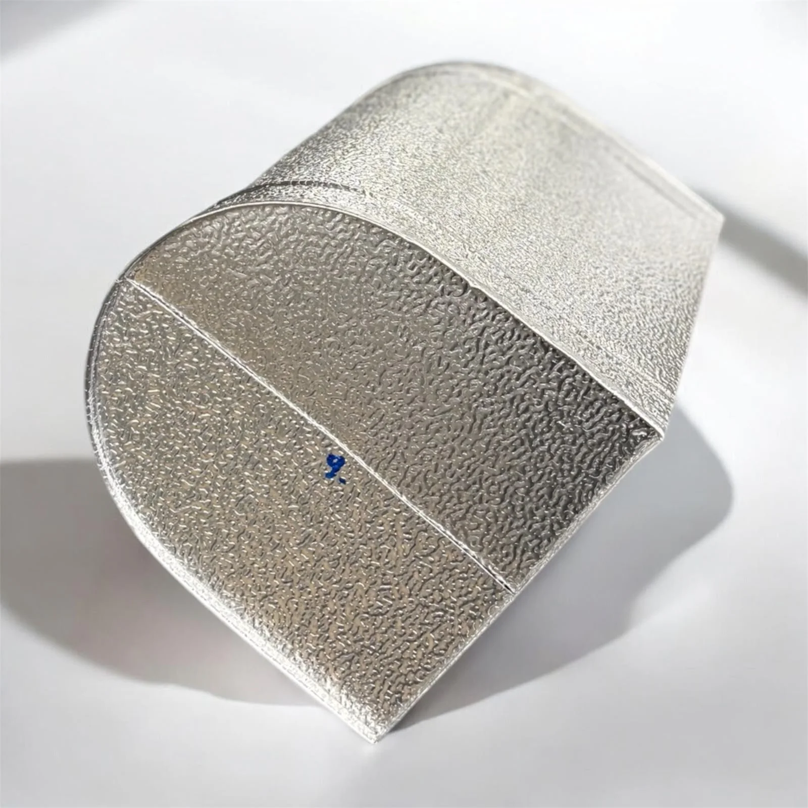 Ein silbernes, metallisches Würfel mit erhabenen, gemusterten Oberflächen auf jeder Seite, auf weißem Hintergrund.