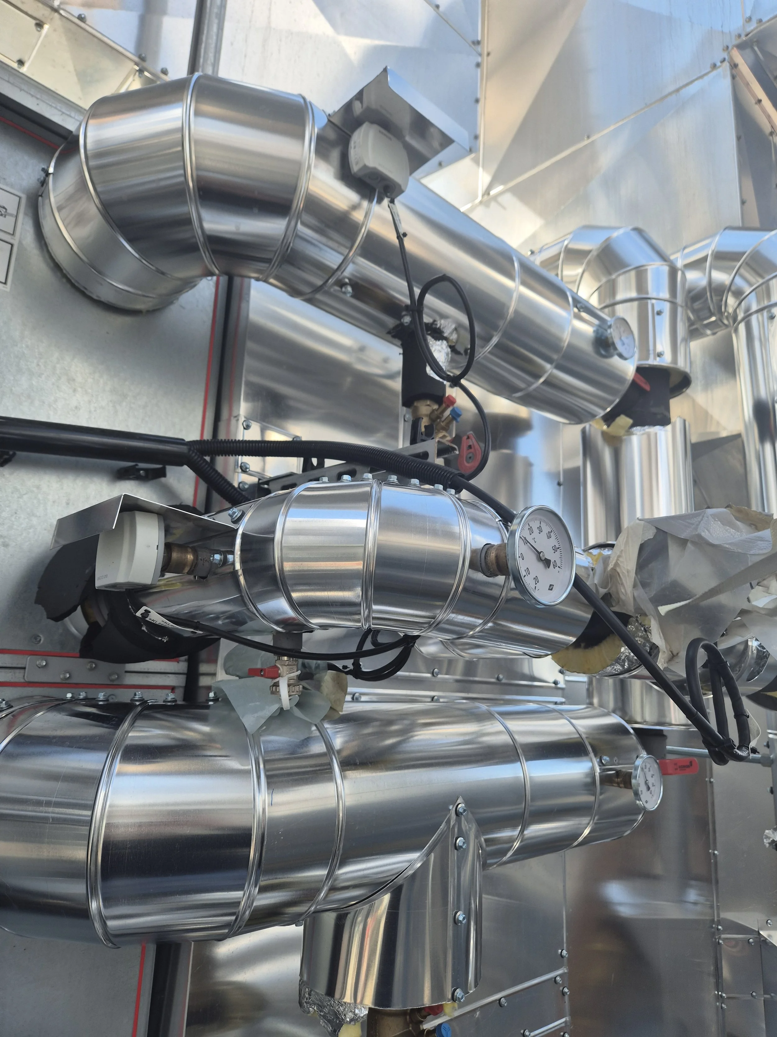 Runde, silberne industrielle Rohrleitungen mit Thermometern und Verbindungselementen in einer technischen Umgebung.