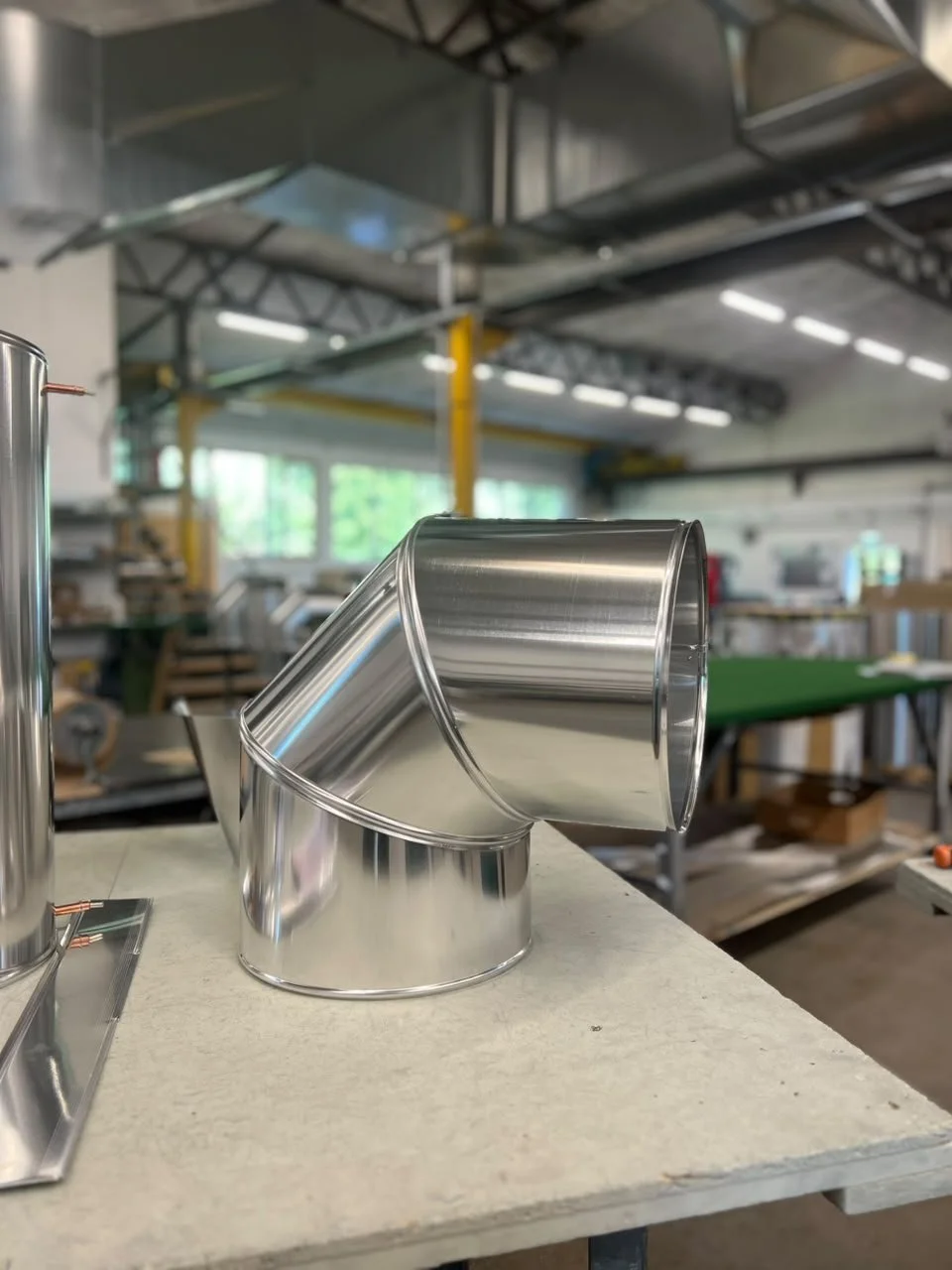 Zwei verchromte Metallrohre auf einem Werkstatttisch, im Hintergrund eine Werkstatt mit Maschinen und Werkzeugen.