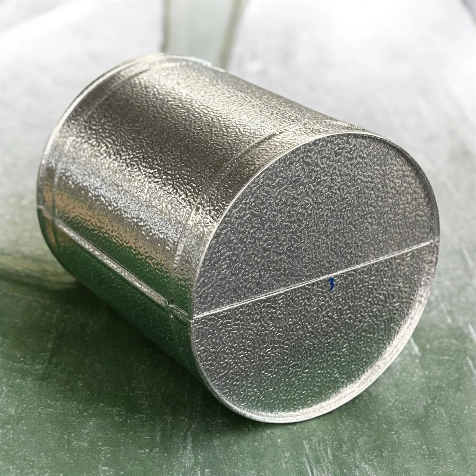 Ein silberner Metallbecher liegt auf einer grünen Oberfläche.