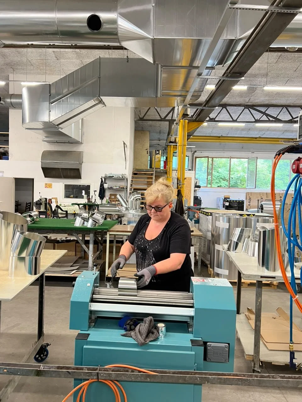 Eine Frau arbeitet in einer metallverarbeitenden Werkstatt und verwendet eine Maschine, um Metallrohre oder -bleche zu schneiden oder zu formen.