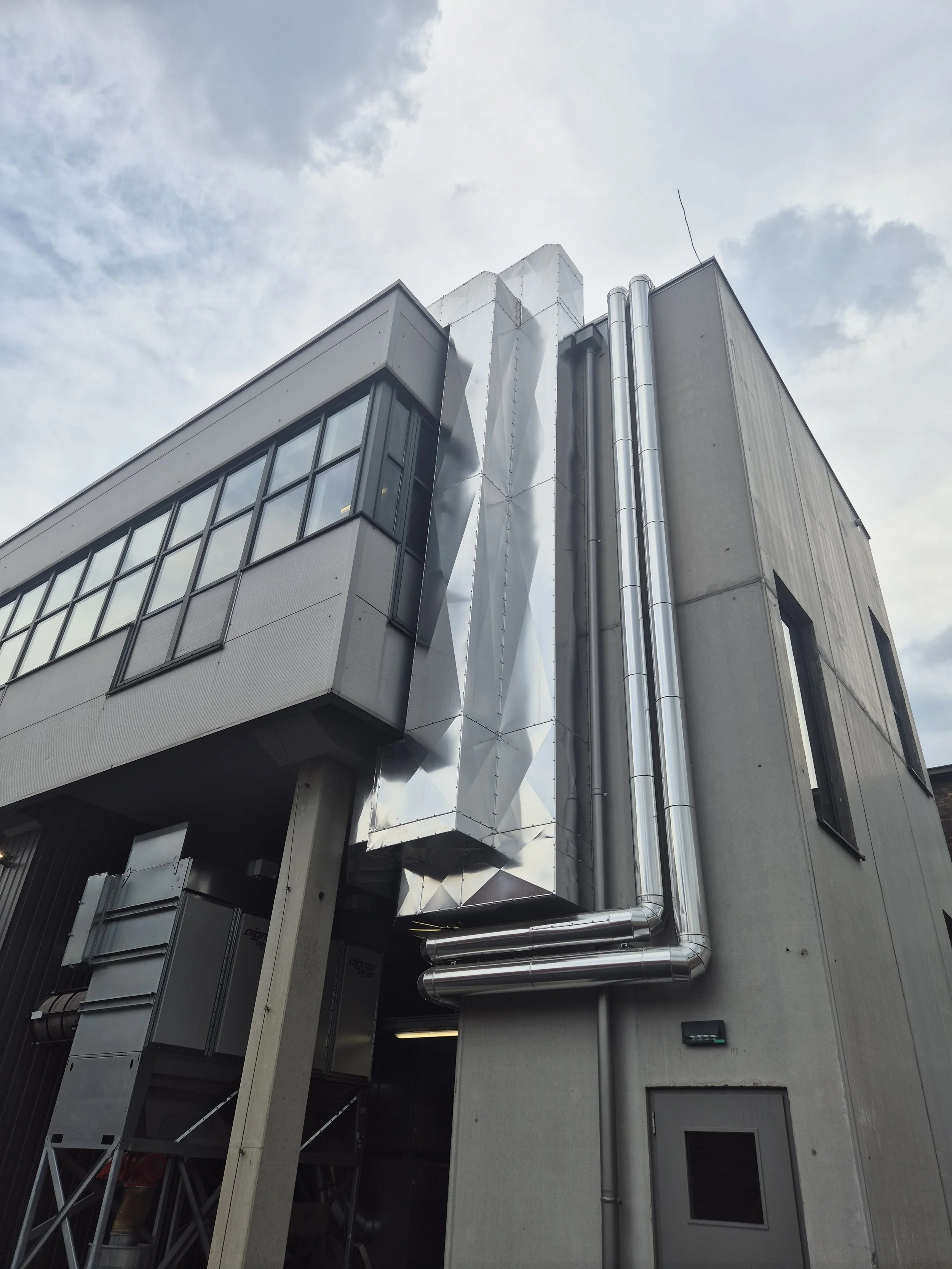 Ein modernes Gebäude mit Fensterfassade und sichtbaren Metallrohren an der Außenwand.