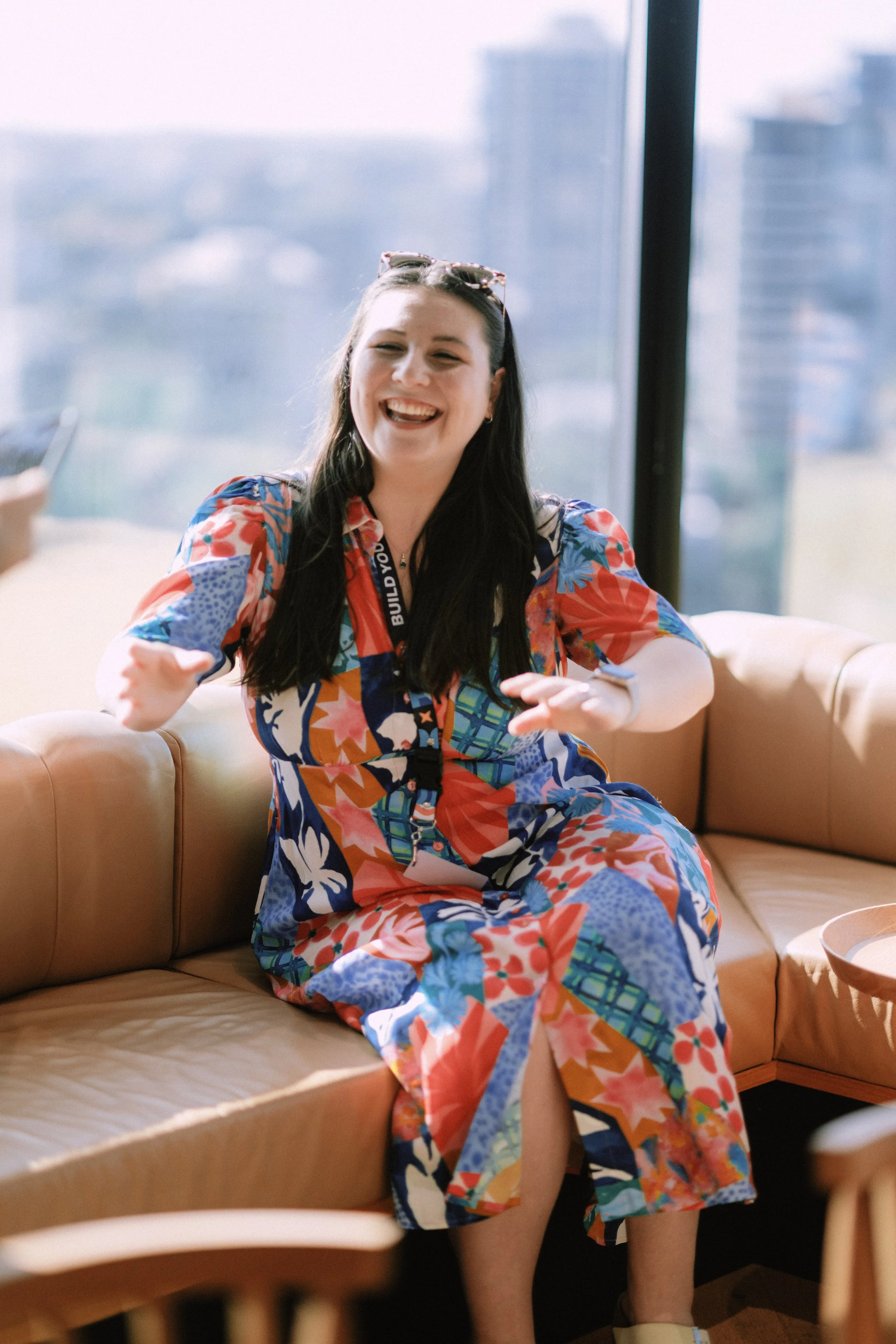 Grace Occleshaw Reaching out to greet her client and start helping their business. Grace wears a colourful floral dress, sunglasses and a broad smile.