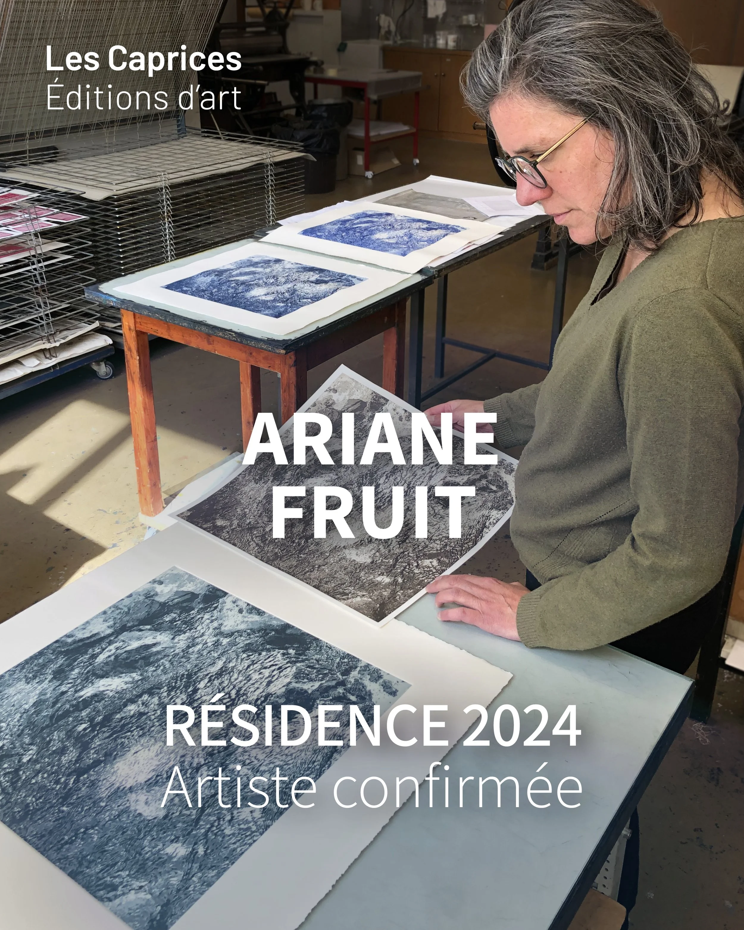 Une femme regarde des impressions d'œuvres d'art sur une table dans un atelier, avec un environnement de travail en arrière-plan.