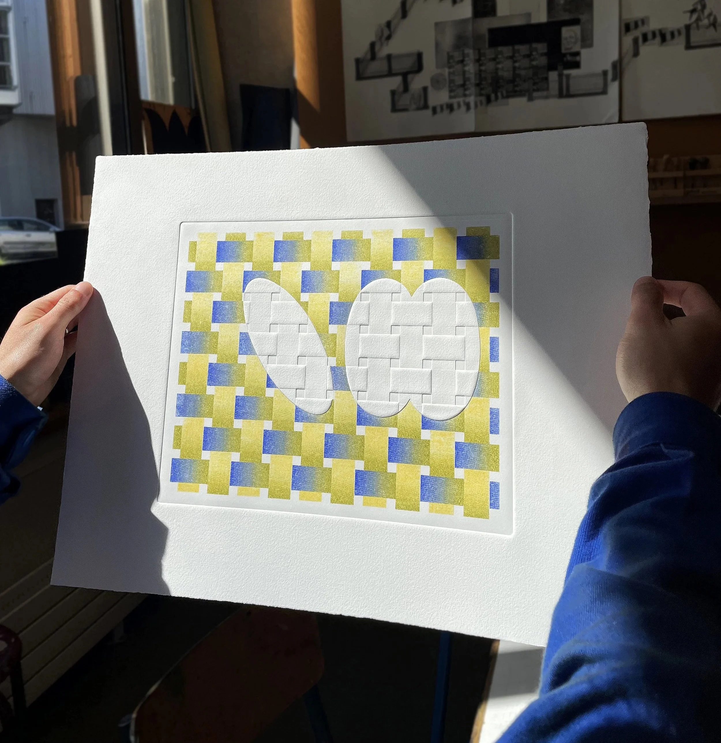 Une personne tient une feuille avec un dessin coloré, dans un espace intérieur.