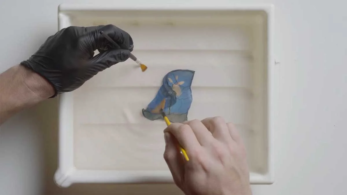 A pair of hands separating the emulsion from the rest of a Polaroid print.