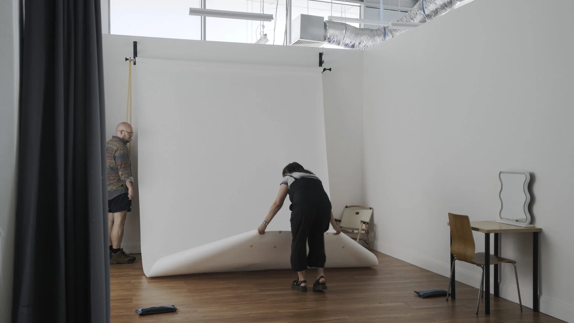 Staff setting up a white paper backdrop in Studio B, demonstrating how the backdrop system can be configured for photography shoots.