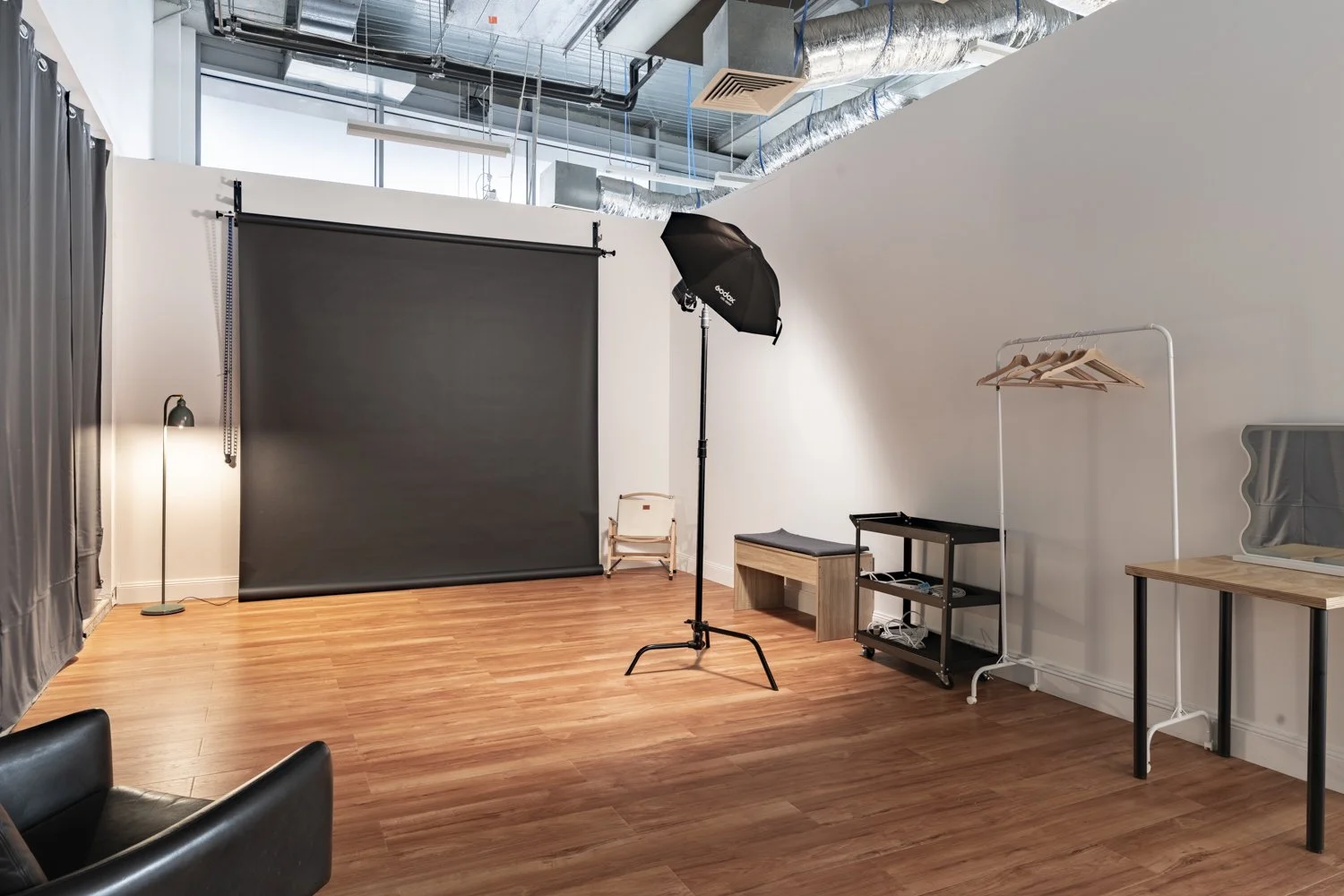 A studio space with floorboards. There is a c-stand with a stronbe light and umbrella on it. There is a black paper backdrop.