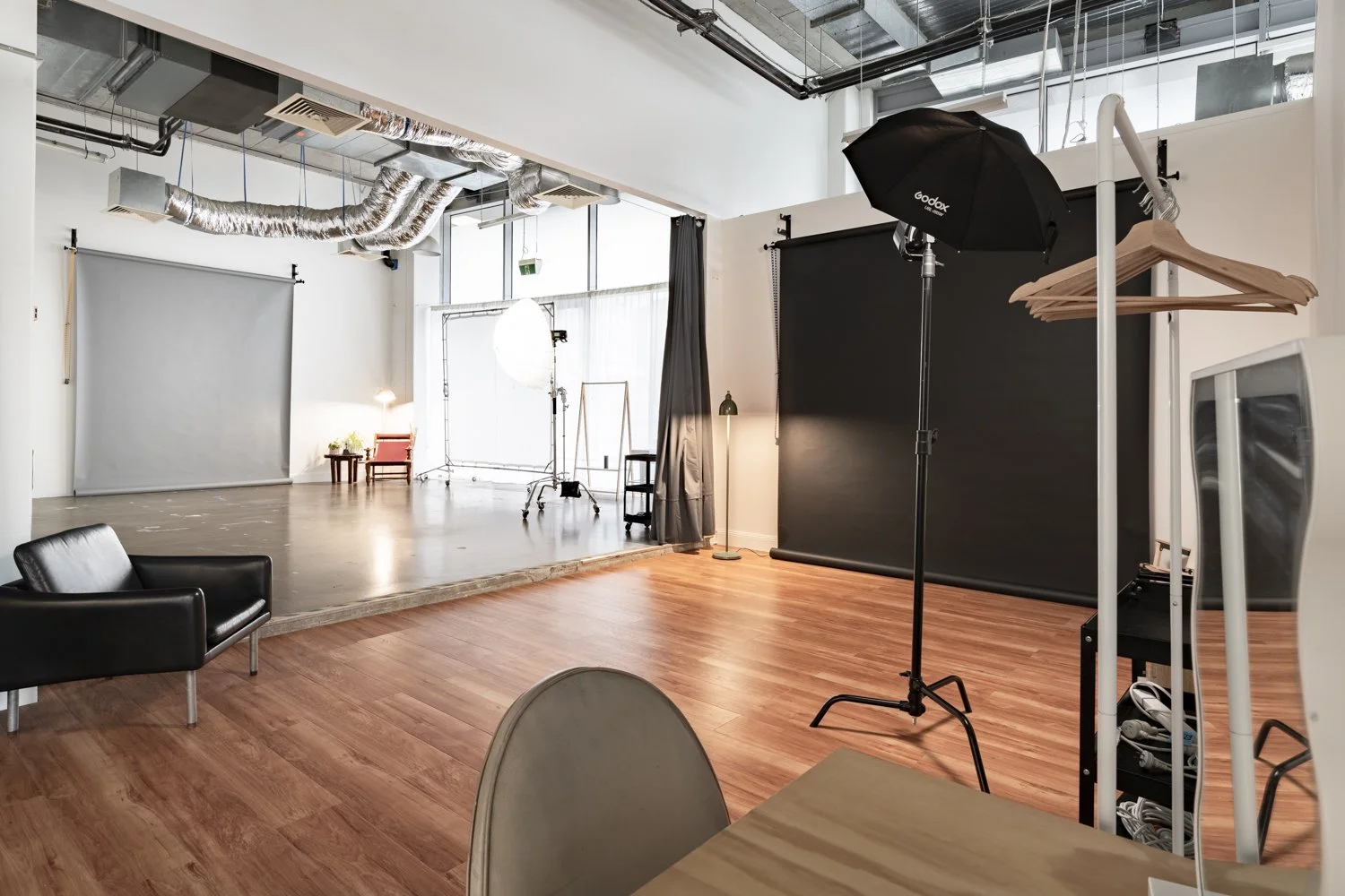 A large photo studio with concrete and floorboards. There are two paper backdrops, one grey and one black. There are strobe lights, modifiers and light stands in each studio.