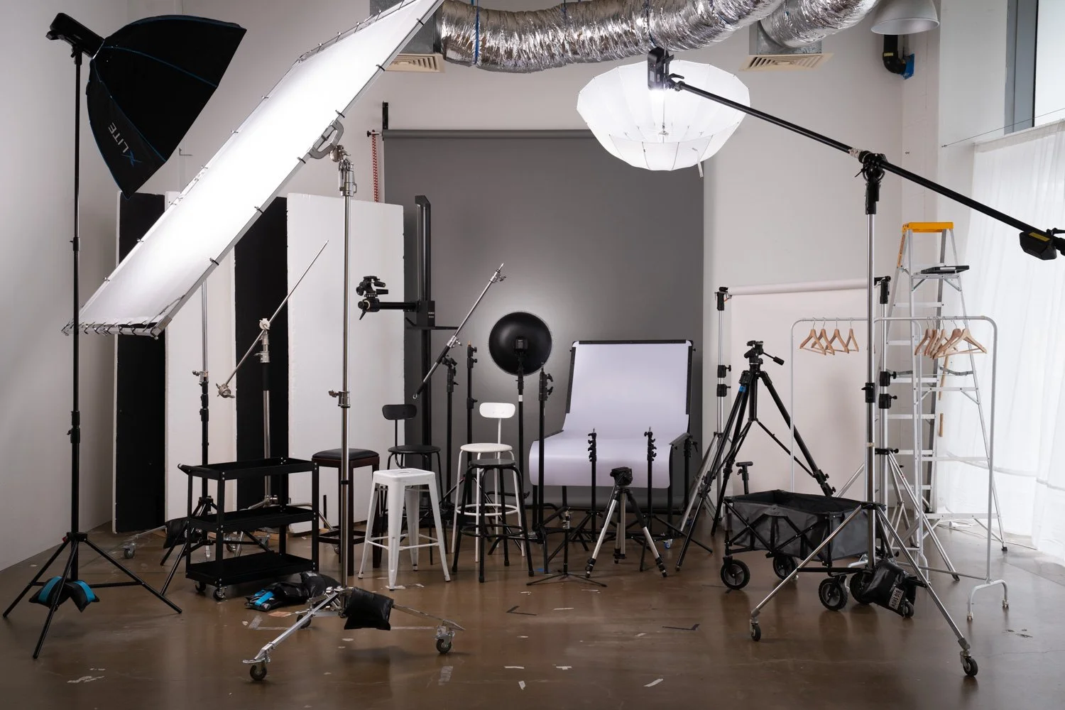 Photography studio setup with softbox lighting, a large diffusion frame, boom-mounted lantern softbox, backdrop system, tripods, c-stands, reflectors, stools and studio grip equipment.