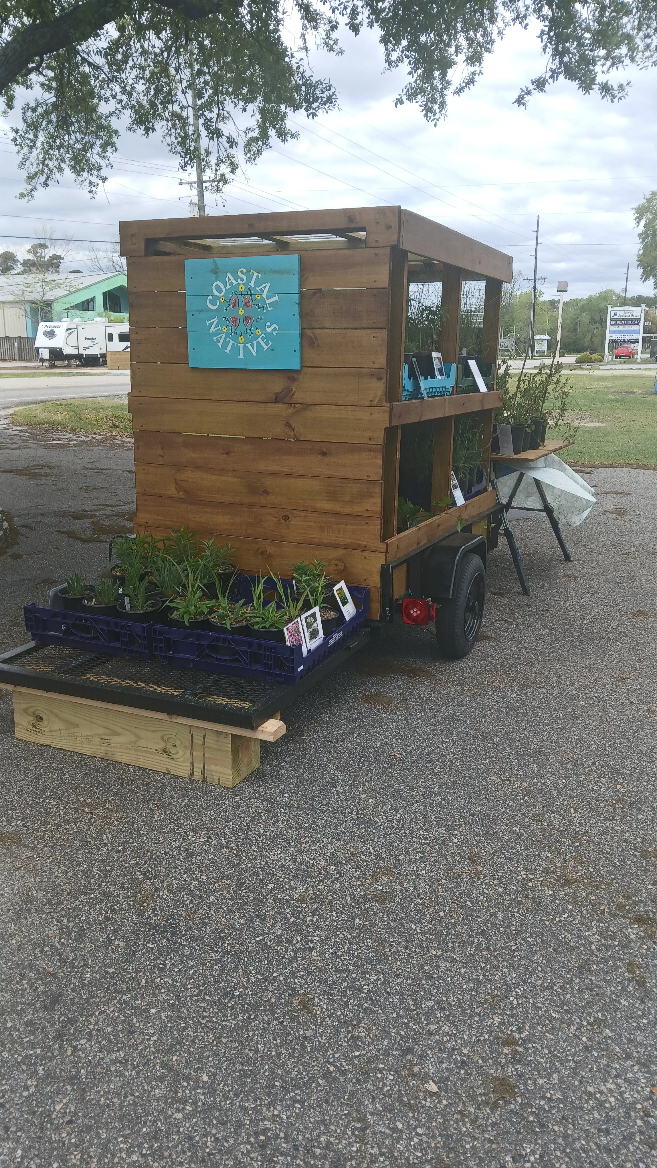 A small wooden mobile stand selling plants and garden items, with a sign reading 'Coastal Natives' on the front.