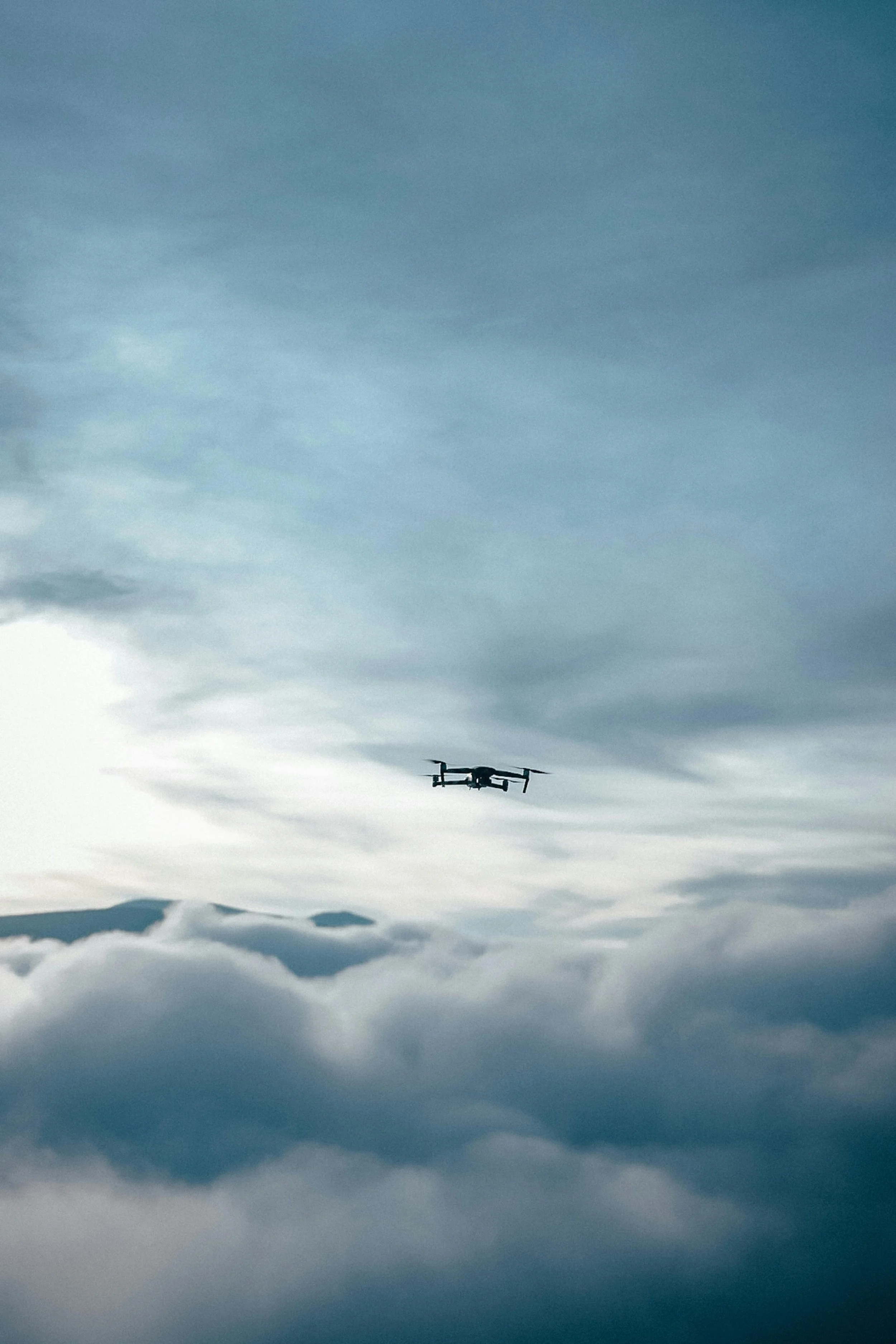 Drone i lufta med tåke og fjell i bakgrunnen