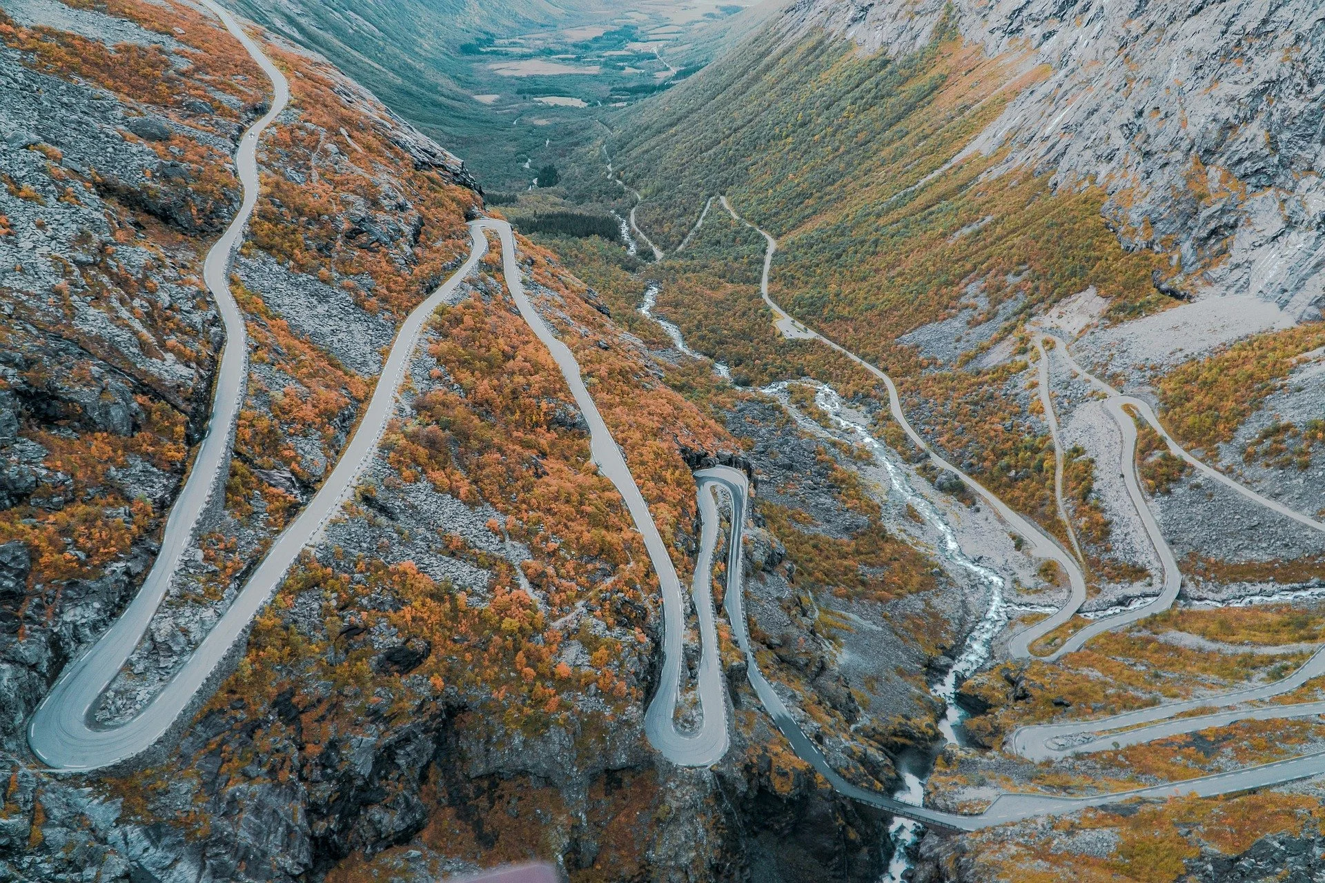 Et fjellandskap med en svingete vei som går oppover fjellsiden, omgitt av høstfargede trær og fjell.