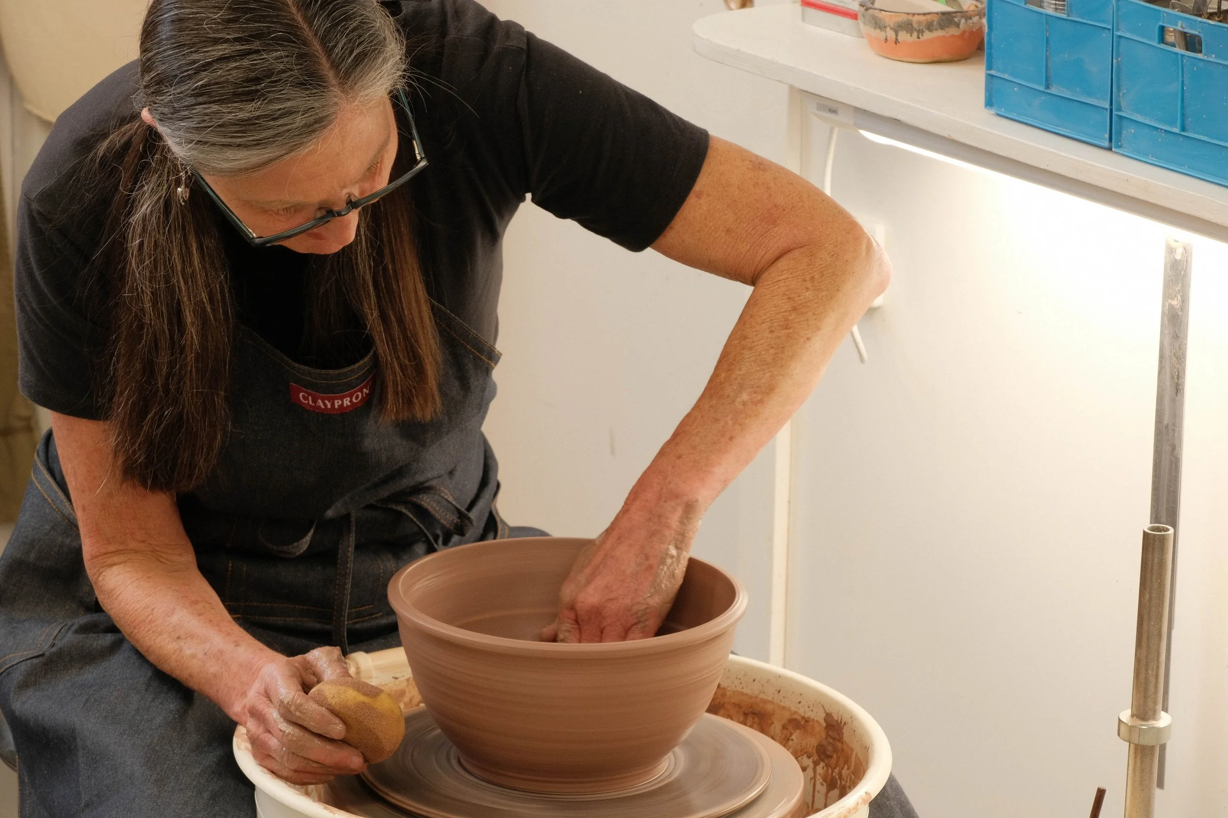 A woman working on a pottery wheel shaping a clay pot in a pottery studio.