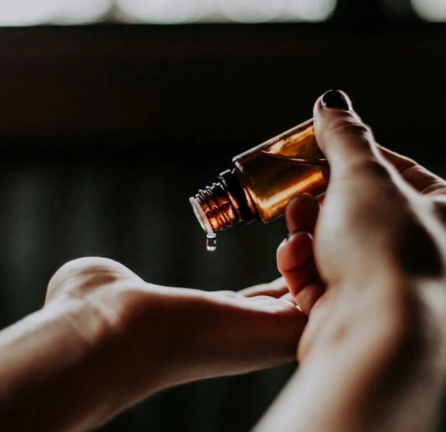 Eine Person gießt eine Flüssigkeit aus einer braunen Flasche in ihre offene Hand.