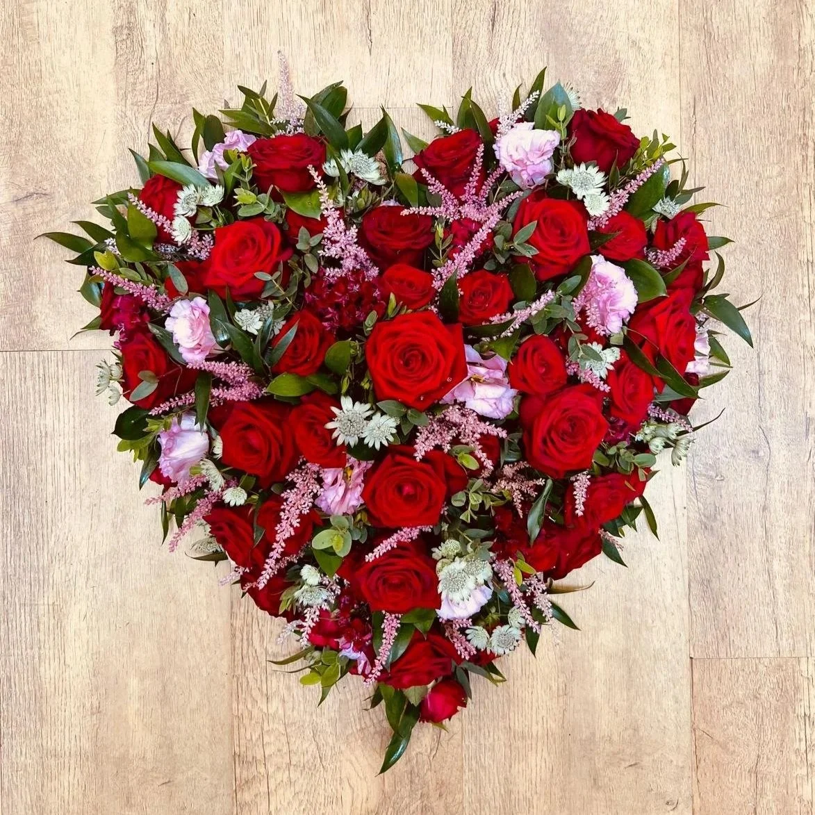 Luxurious Red Rose and Pink Astilbe Solid Heart | A striking and deeply expressive solid heart arrangement styled with a loose, natural texture. Breaking away from a traditional flat base, this heart is completely filled with a dense, lavish mix of r