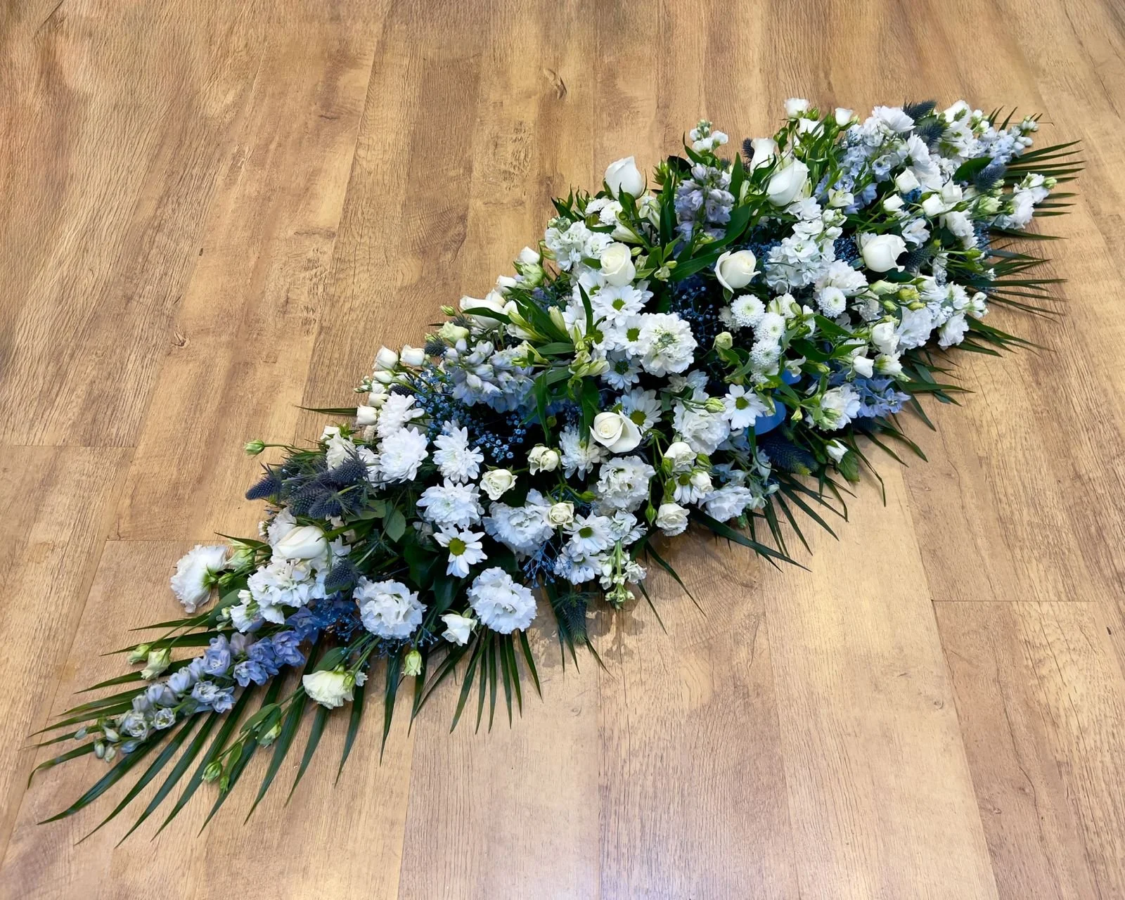 Classic Navy Blue & White Spray | A deeply tranquil and soft arrangement blending snowy white roses and lisianthus with gentle blue delphiniums and thistle accents. Clusters of tiny white filler flowers give it a light, cloud-like texture, perfectly 