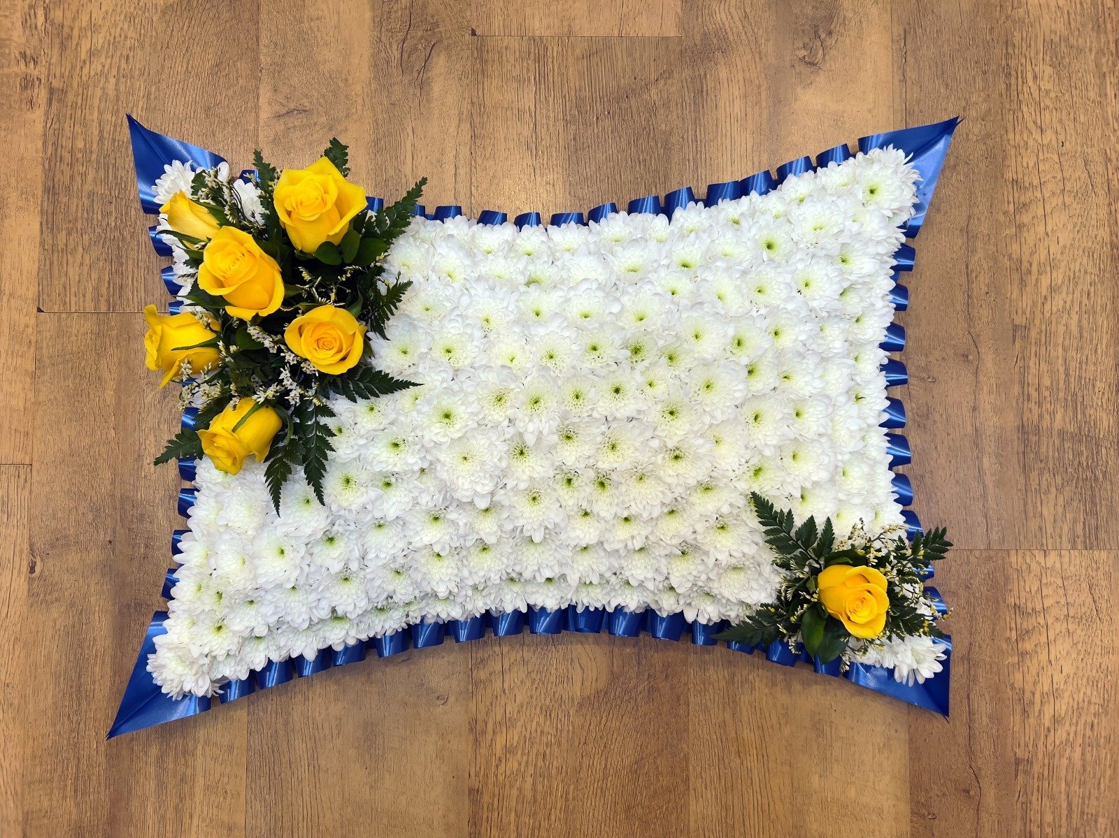 Canary Yellow and Royal Blue Floral Pillow | A peaceful and comforting pillow-shaped tribute. The cushion is densely packed with a flawless base of white chrysanthemums, dramatically framed by a vibrant royal blue pleated ribbon border that forms sha