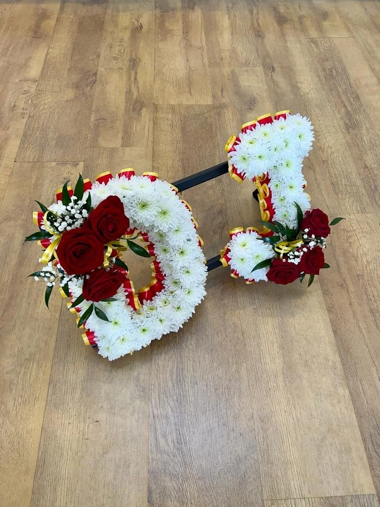 Red Rose and White Chrysanthemum Tribute | A classic and elegant two-letter tribute spelling "DJ". The letters are densely based with clean white chrysanthemums, framed beautifully by a pleated red and gold ribbon border. Striking clusters of deep re