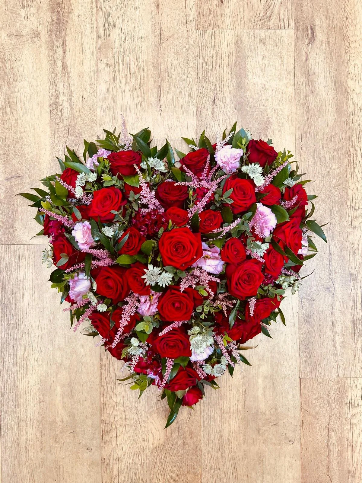 Luxurious Red Rose and Pink Astilbe Solid Heart | A striking and deeply expressive solid heart arrangement styled with a loose, natural texture. Breaking away from a traditional flat base, this heart is completely filled with a dense, lavish mix of r