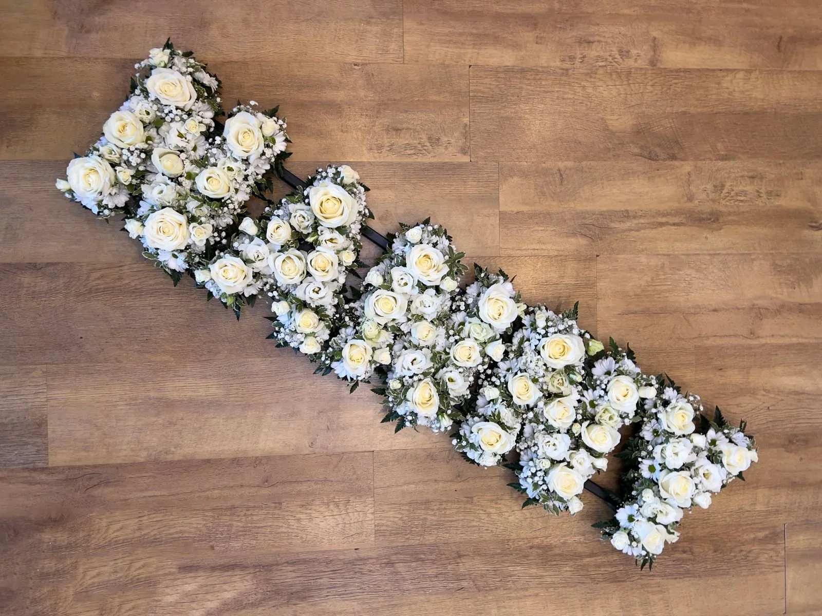 All White Flowers Tribute | A luxurious, fully textured tribute spelling "NANNY". Departing from the traditional flat chrysanthemum base, every letter in this arrangement is intricately packed with open white roses, cream spray roses, and frothy whit