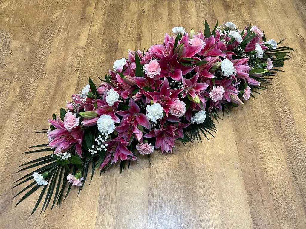 Pink and White Elegance Spray | A beautiful and classic tribute featuring a dense arrangement of vibrant fuchsia-pink lilies, balanced elegantly with soft pink and crisp white carnations. Delicate sprays of white gypsophila (baby's breath) are nestle