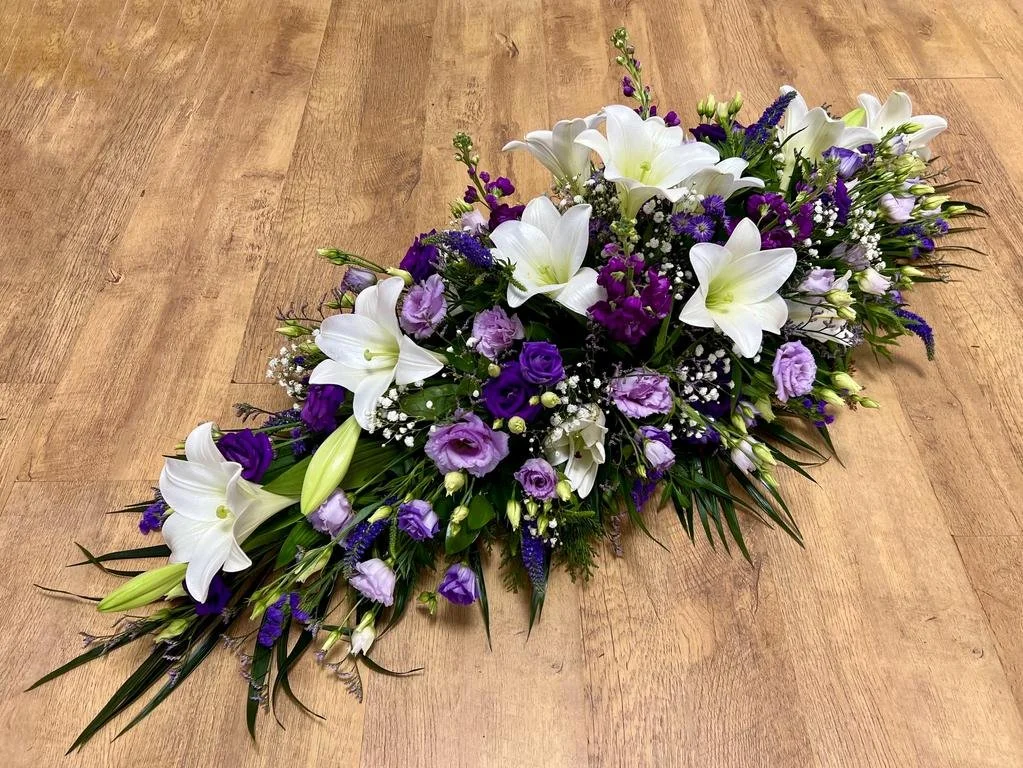 Royal Purple and White Lily Spray | This striking arrangement combines large, pristine white lilies with a rich palette of purples. It features deep violet lisianthus, soft lavender blooms, and upright purple stocks, accented by delicate white filler