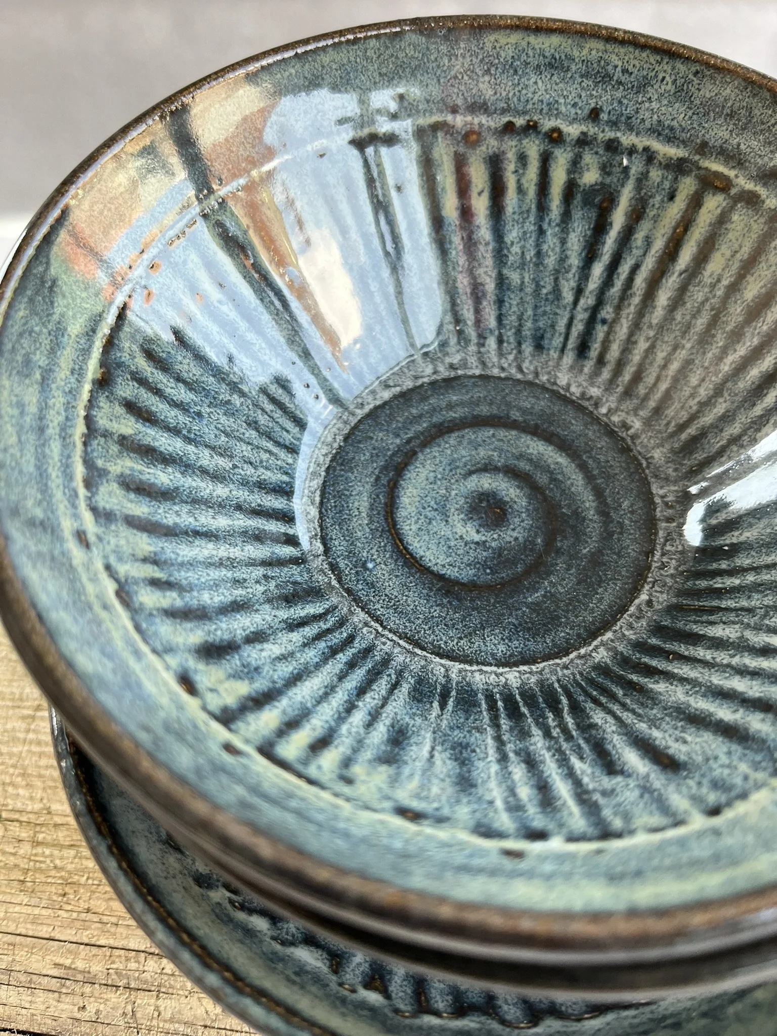 Close-up of a ceramic bowl with a textured, glazed interior in shades of blue, green, and brown, sitting on a wooden surface.