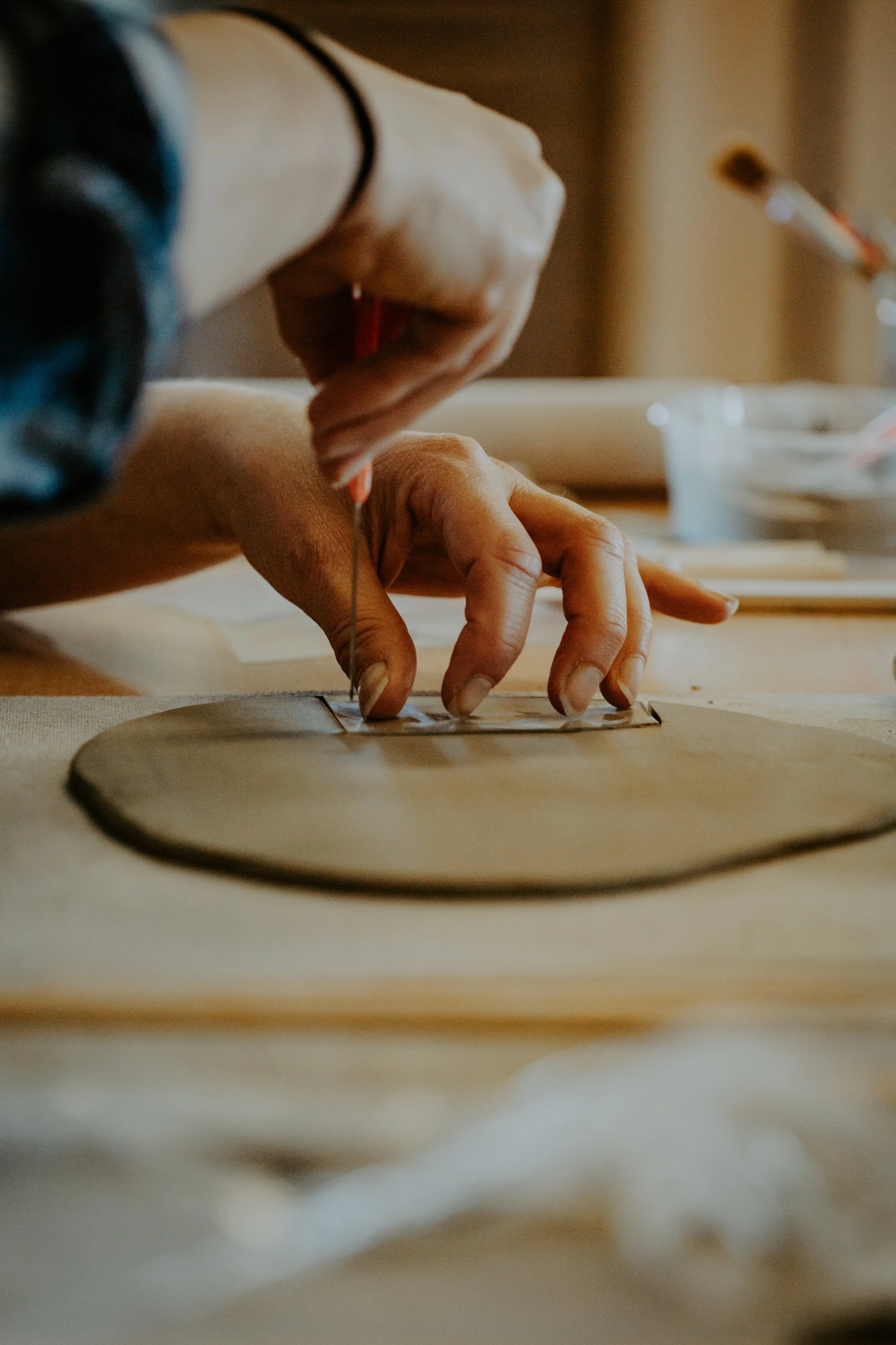 Close-up of a person sewing or crafting, with their hand holding a tool and cutting clay in the background.