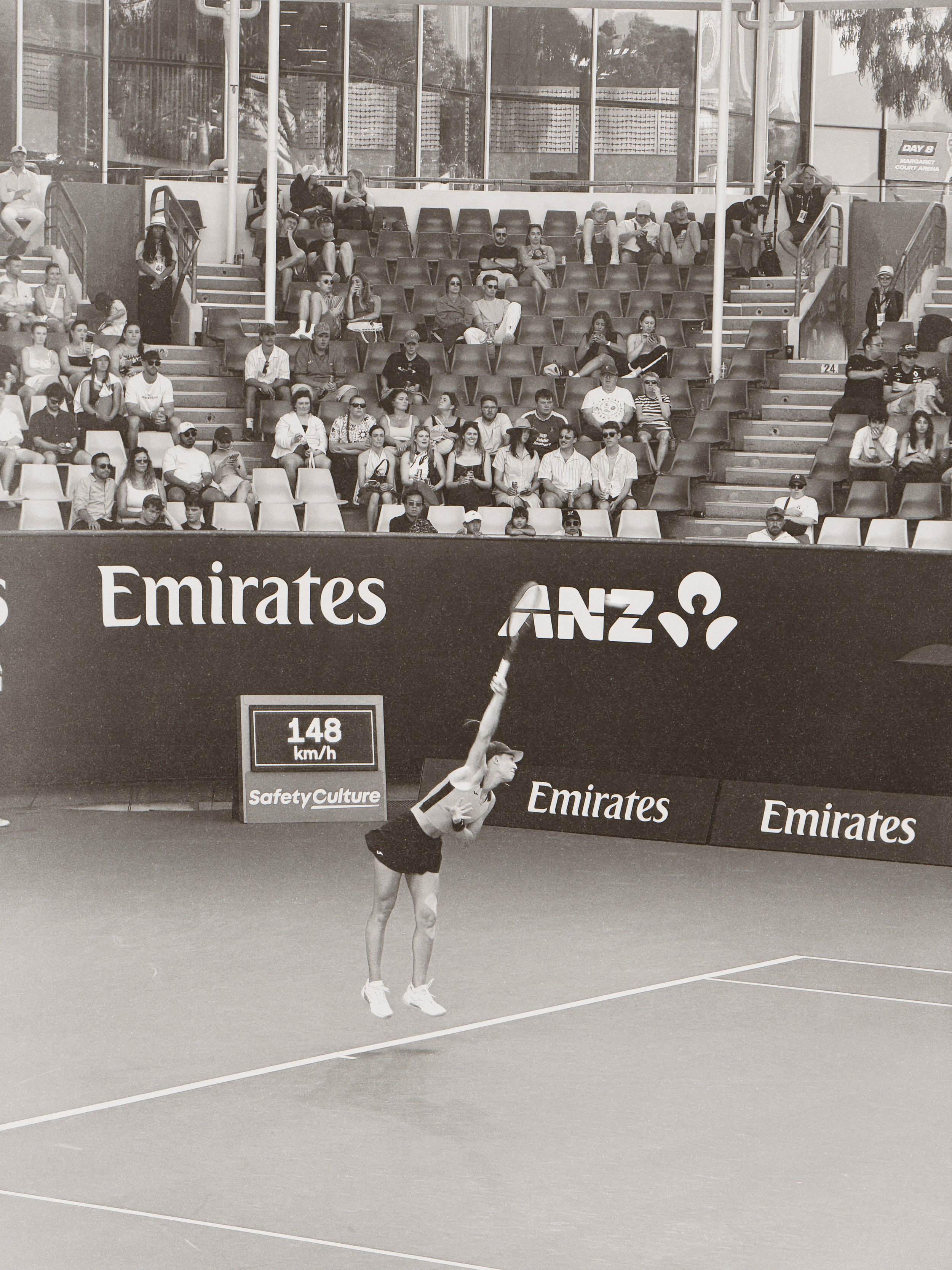 A woman in athletic clothing and sneakers performing a tennis serve on a tennis court with a large audience watching from the bleachers.