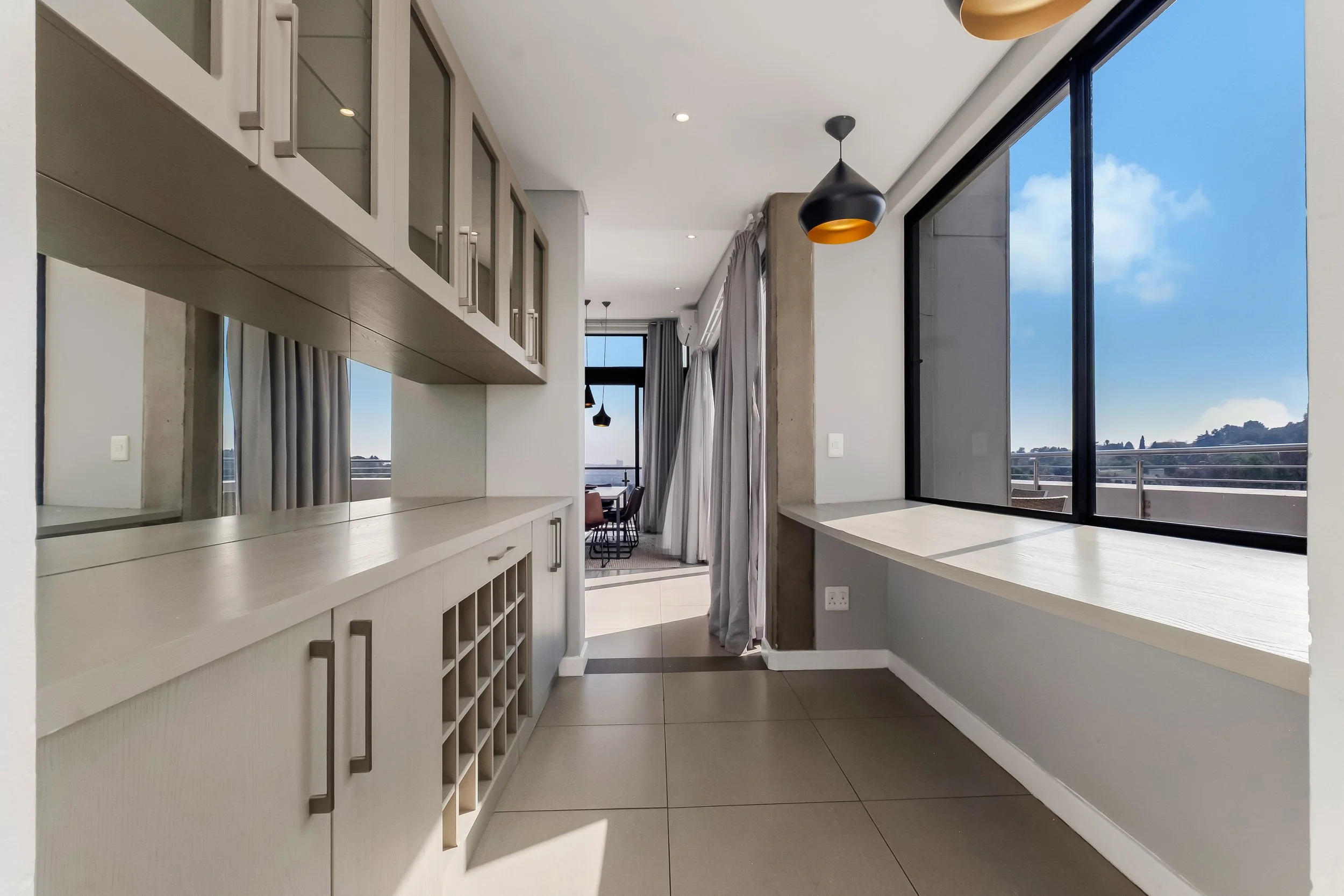 Modern kitchen with white cabinets, large window, and a view of blue sky and hills.