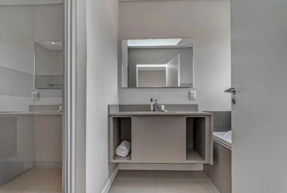 Modern bathroom with a gray vanity, large mirror, and a towel stored underneath, alongside a bathtub on the right and a shower on the left.