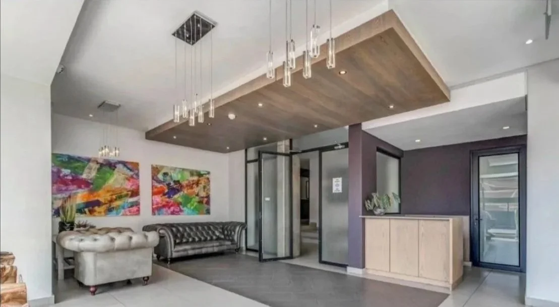 Interior of a modern lobby with abstract paintings on the wall, leather couches, a doorway, and a reception desk.