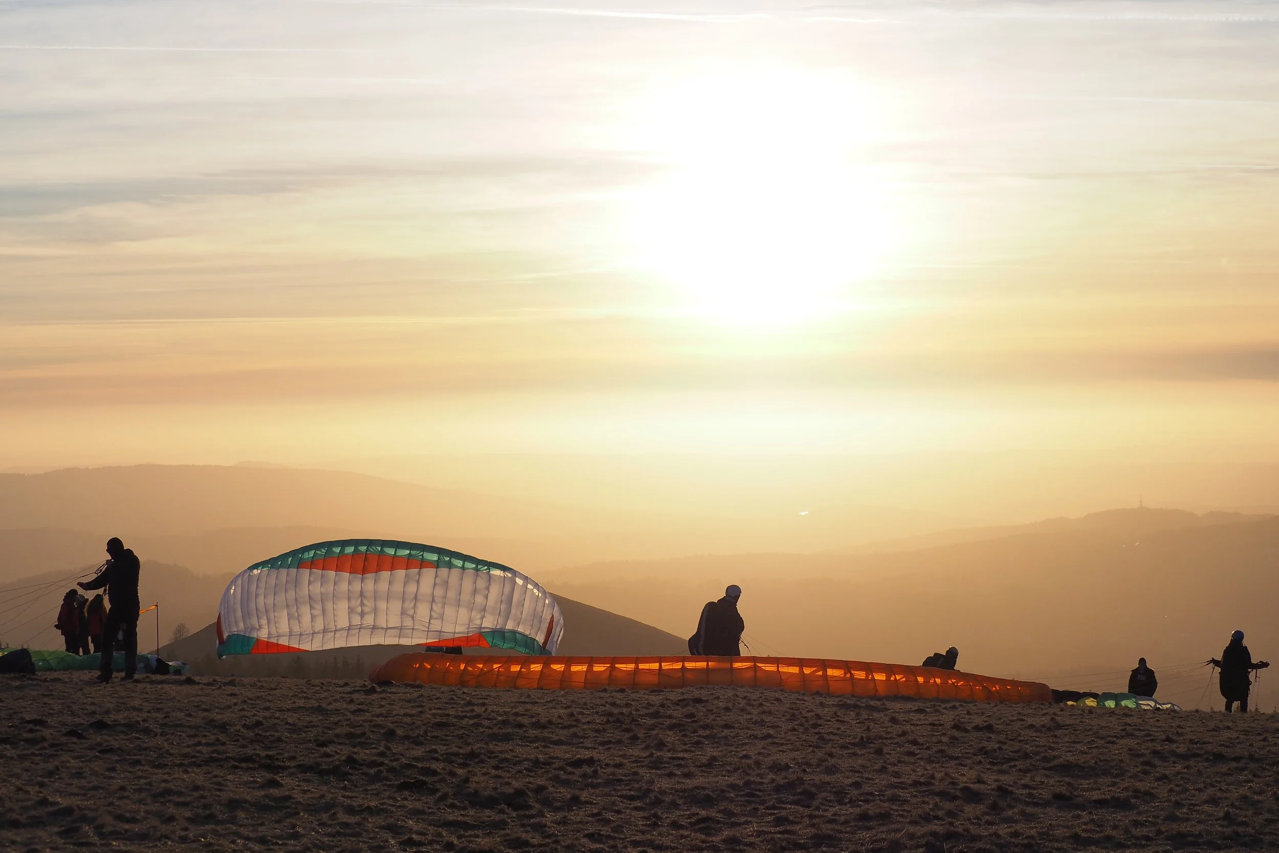 Menschen bereiten sich auf einen Heißluftballonflug bei Sonnenaufgang vor, mit mehreren bunten Ballons am Boden und die Sonne scheint am Himmel.