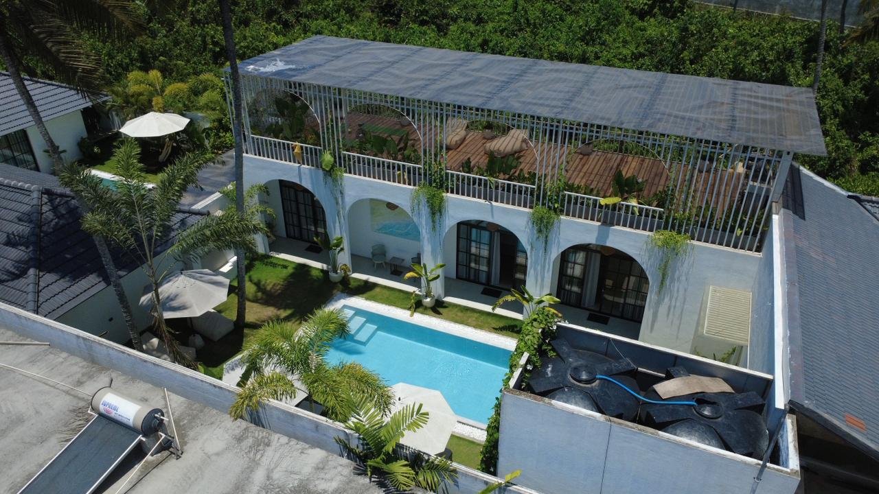 Aerial view of a modern residential building with a swimming pool, outdoor seating area, and rooftop terrace with seating and plants, surrounded by greenery.
