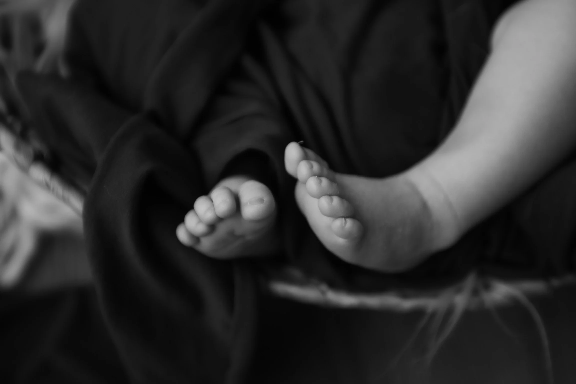 Close-up of a person's hand holding a baby's foot in black and white.
