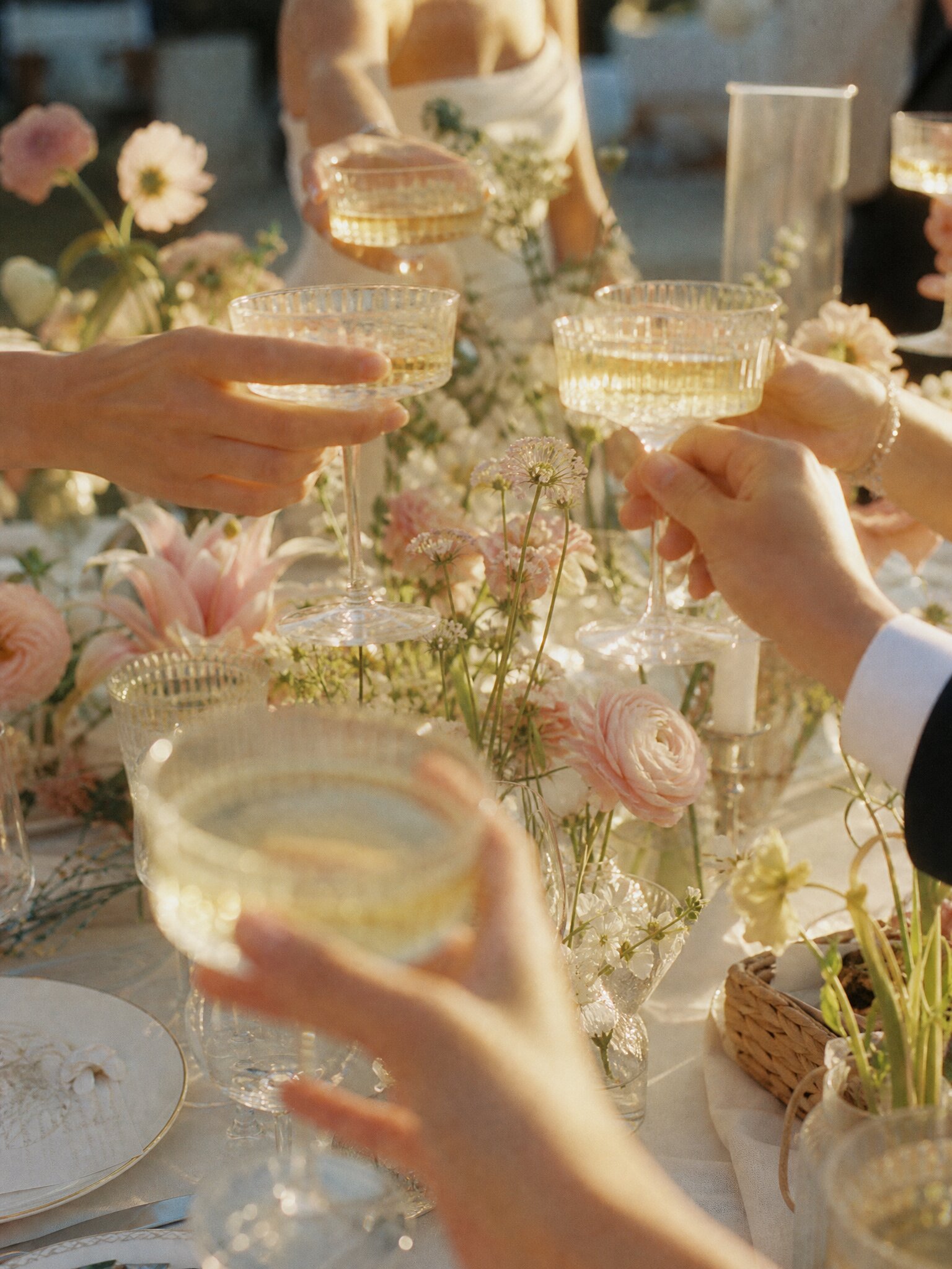 People raising champagne glasses in a toast at a celebration with floral decorations and tableware.