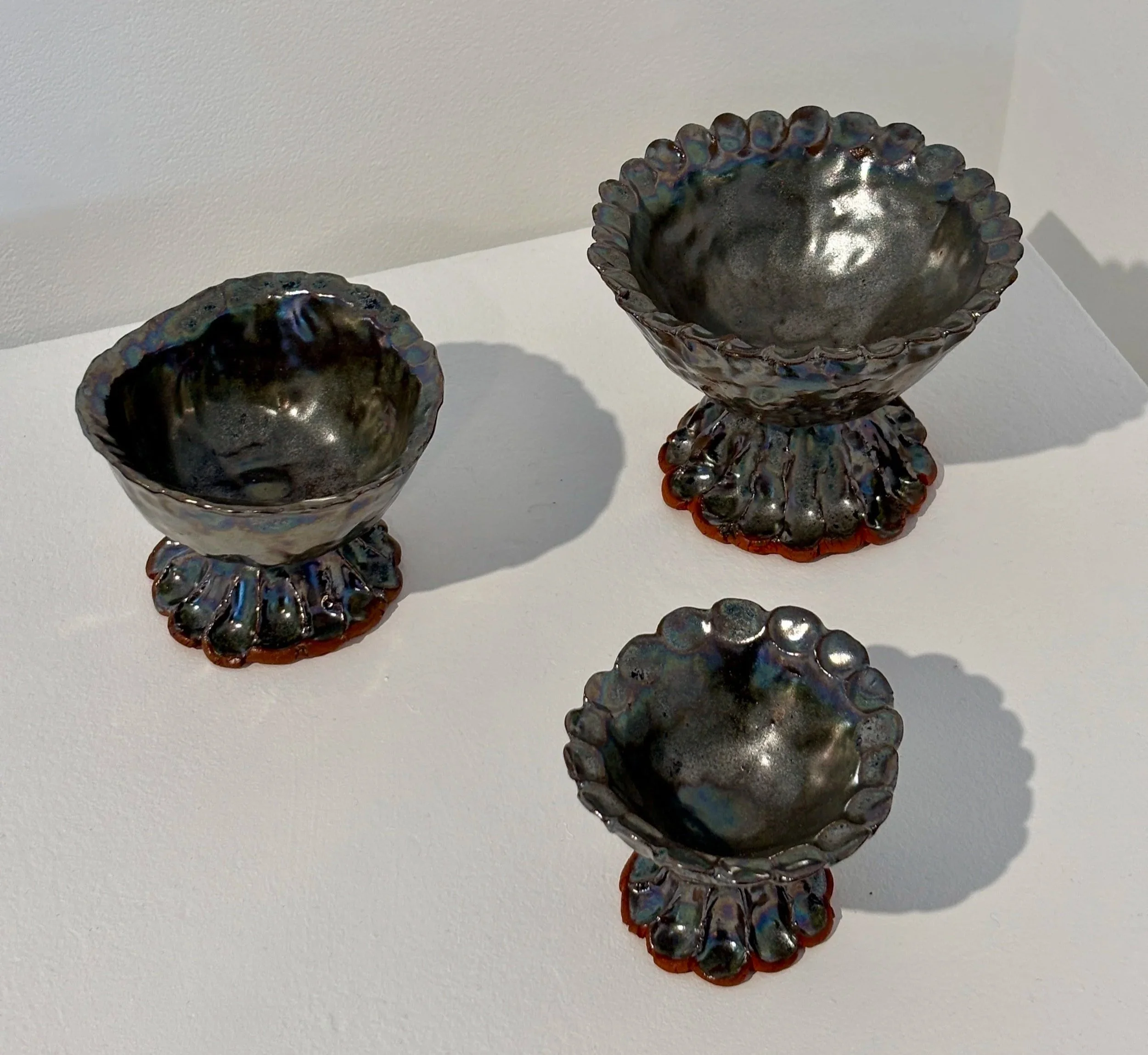 Glass art vessels with iridescent finish and decorative bases, displayed on a white surface.