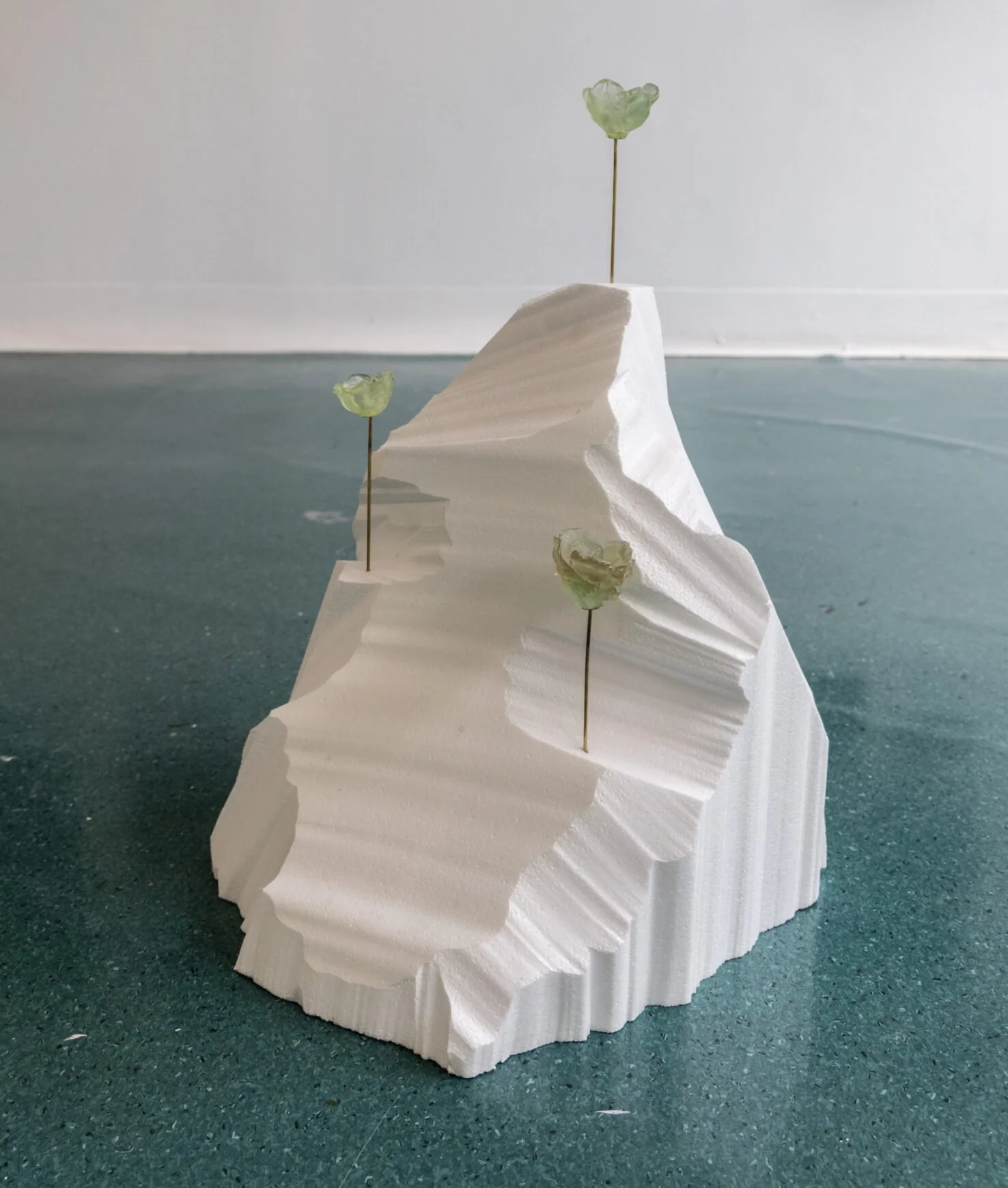 White foam sculpture resembling a mountain with three green rock candy lollipops on thin sticks placed on it.