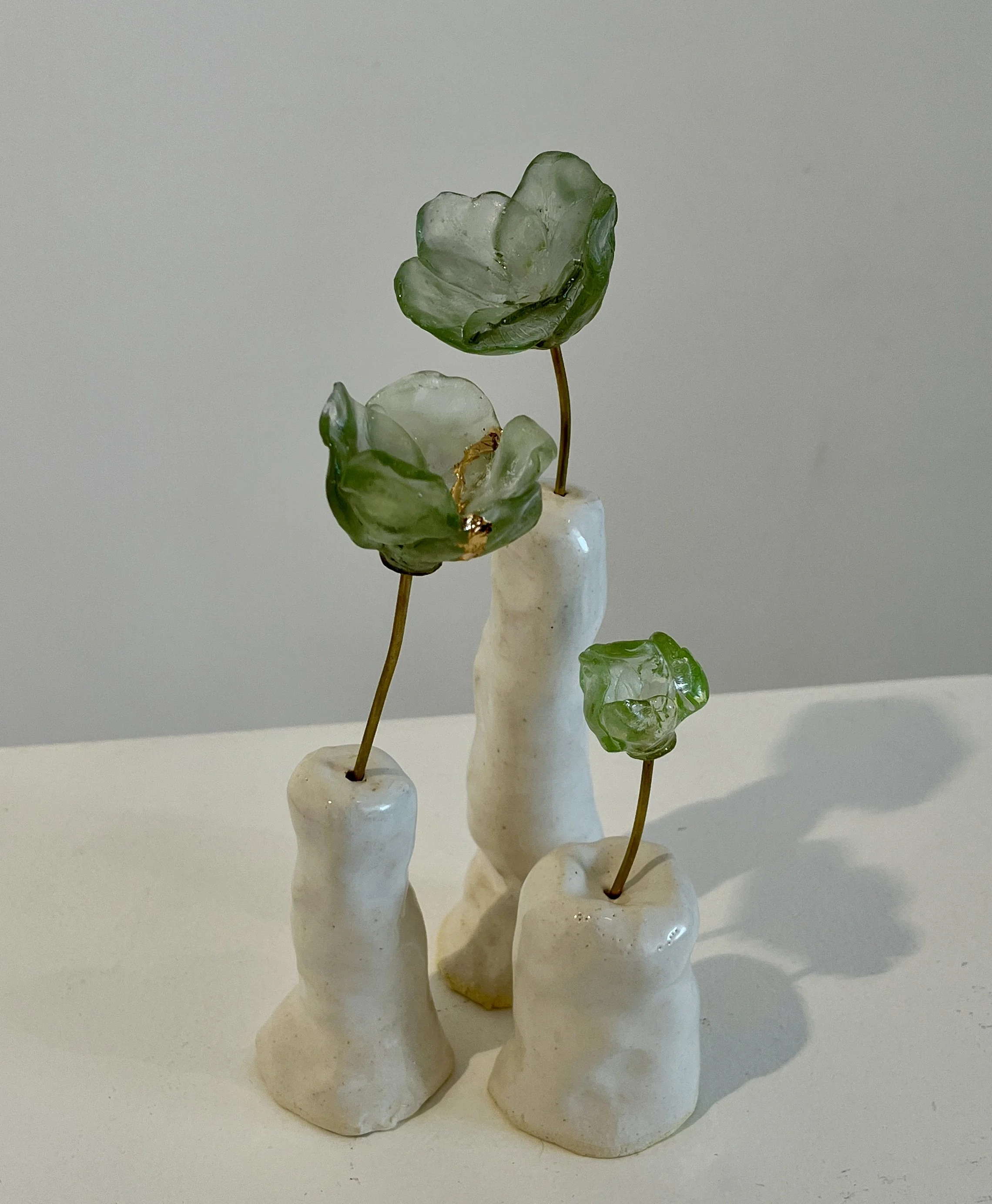 Display of three handcrafted ceramic vases with elongated, irregular shapes, each holding a glass cast flower, set against a plain white background.