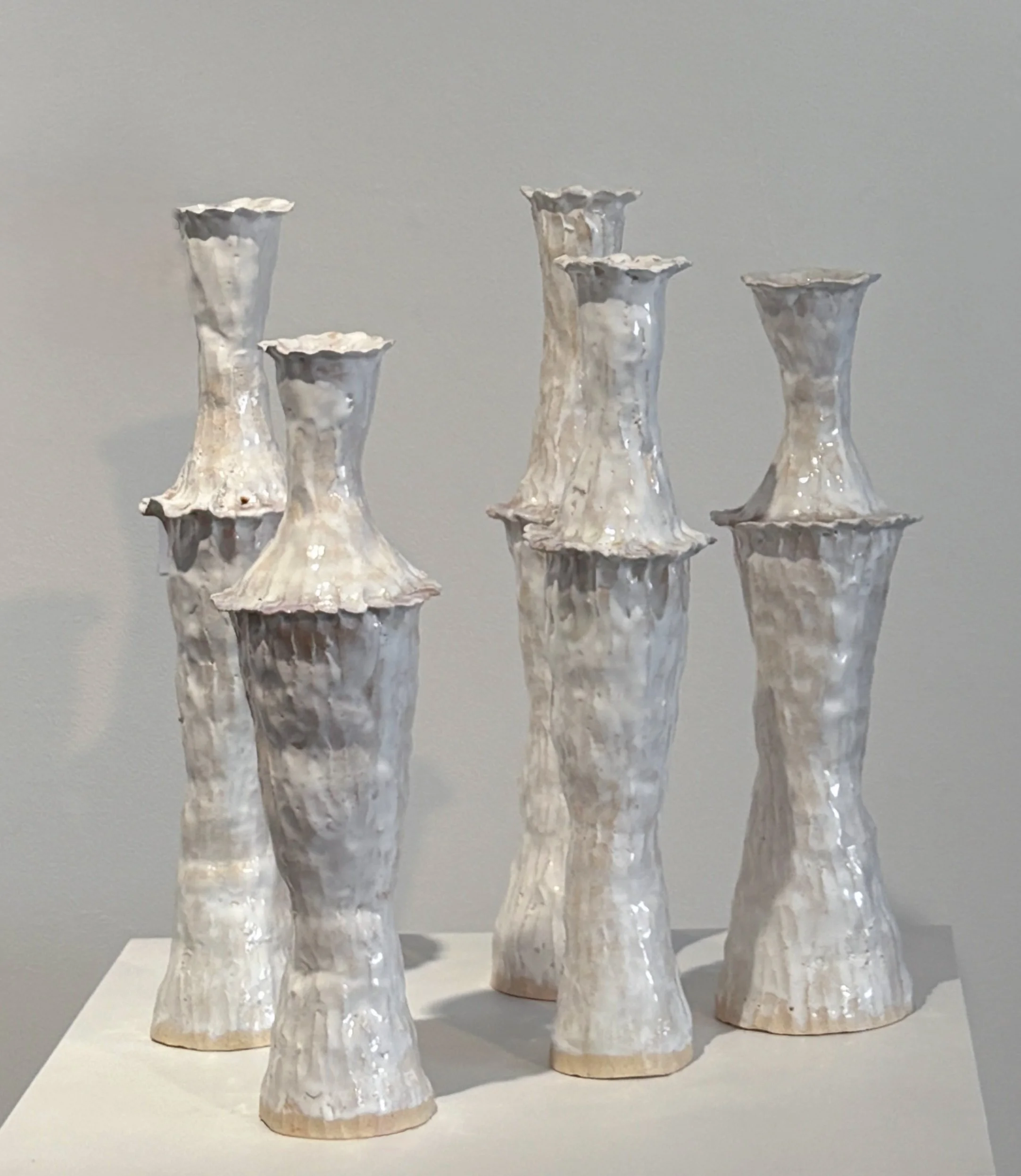 Five ceramic vases with flared tops and textured surfaces, arranged on a white surface against a plain background.